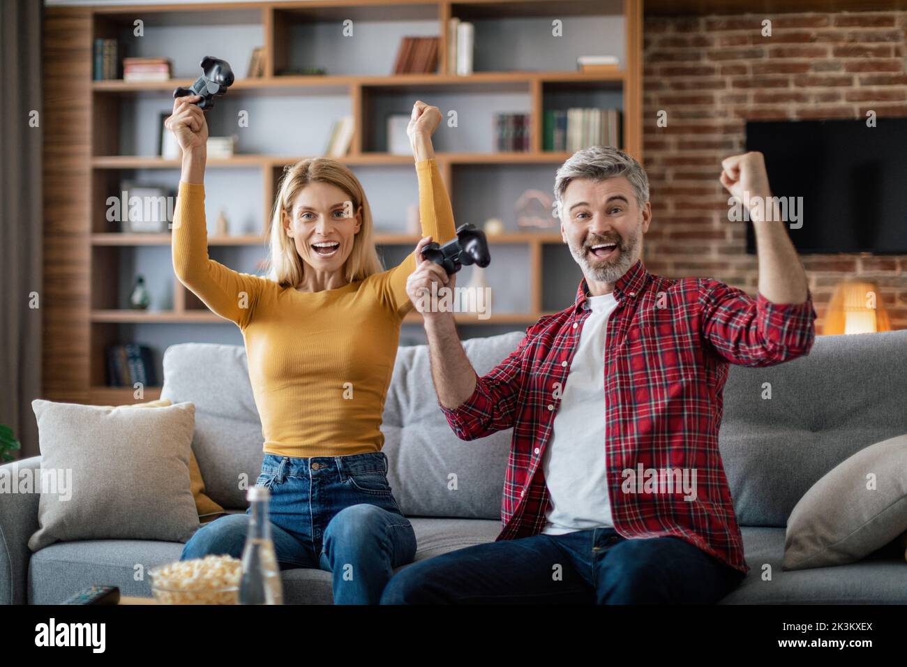 Zufriedene reife europäische Familie mit Joysticks genießen Online-Spiel auf Computer machen Siegesgeste Stockfoto