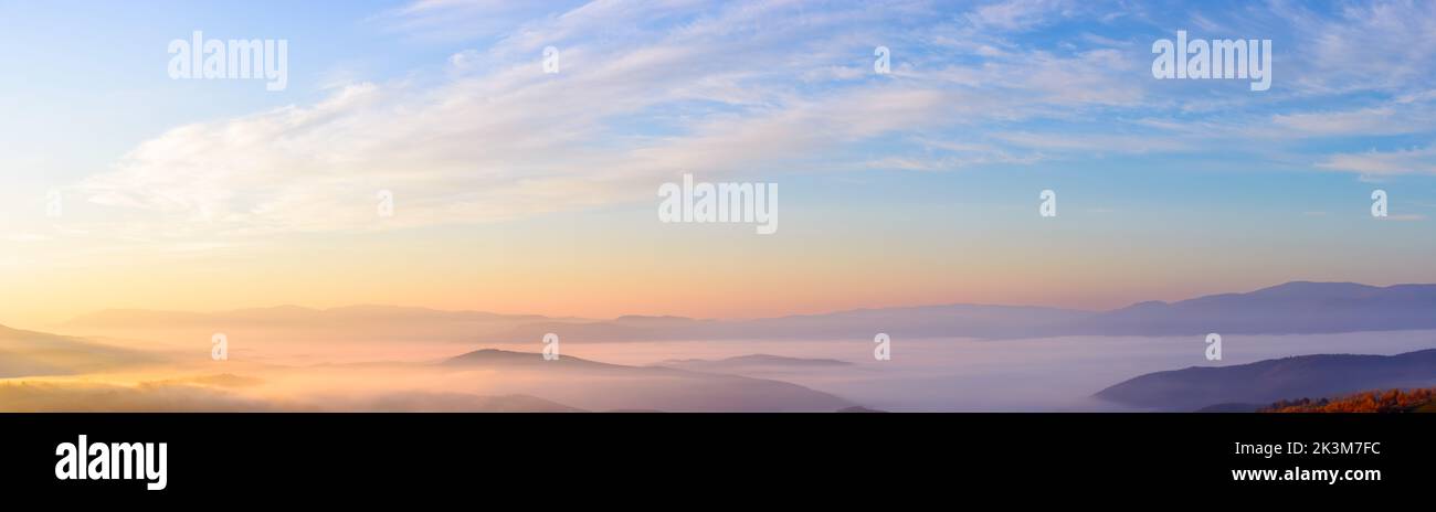 Berglandschaft bei Sonnenaufgang in der Herbstsaison. Ländliches Tal voller glühendem Nebel. Schöne Naturlandschaft im Morgenlicht. Wunderschöne Cirrus Cloudscap Stockfoto