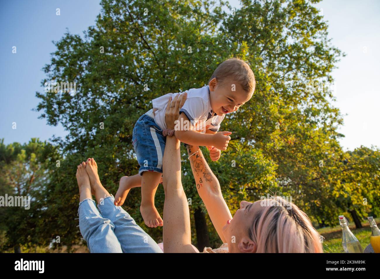 Die junge Mutter spielt mit dem Sohn, indem sie ihn während des Picknicks in die Luft hebt. Muttertag. Stockfoto