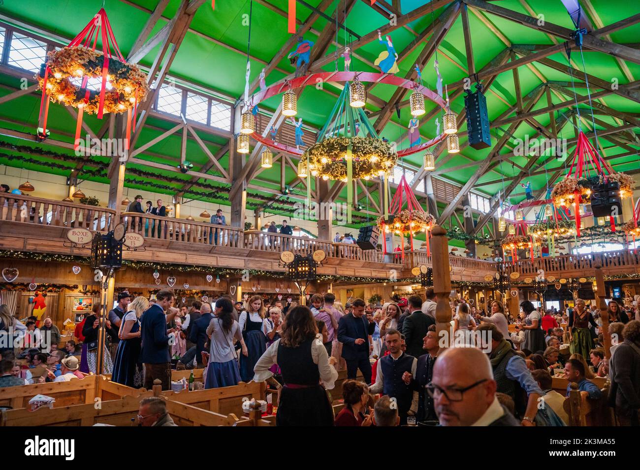Menschen sitzen im Bierzelt auf dem Oktoberfest München. Fröhliche Menschen beim Biertrinken beim weltberühmten Volksfest feiern und zu bayerischer Musik tanzen Stockfoto