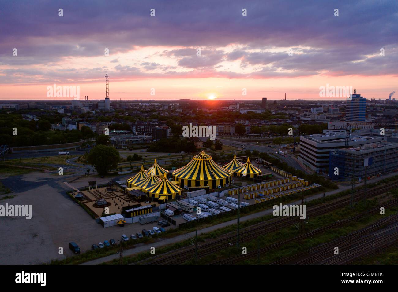 Luftaufnahme des Stadtbildes mit modernen Gebäuden und Zirkuszelten, die bei Sonnenuntergang in Deutschland in der Nähe der Straße aufgestellt wurden Stockfoto