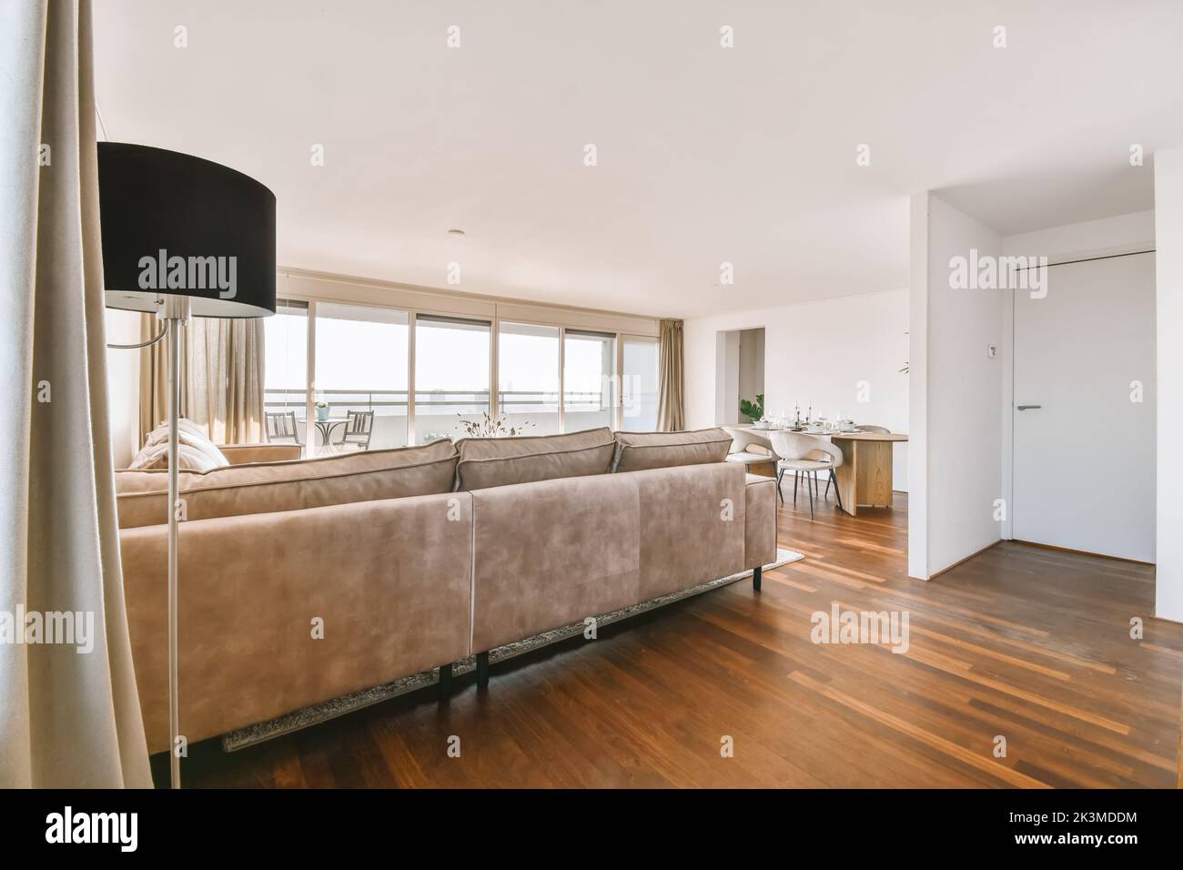 Die Einrichtung einer modernen, offenen Wohnung in Pastelltönen mit Esstisch und Sofa im Wohnzimmer und Küche mit großen Glastüren, die zu b führen Stockfoto