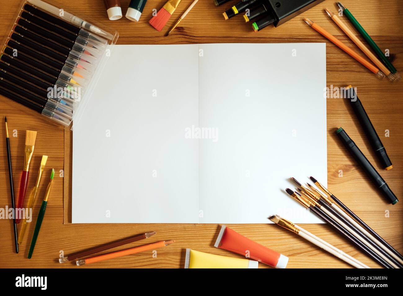 Kreativer Künstler mockup Arbeitsplatz auf Holztisch . Flachlage, Draufsicht mit leerem Skizzenbuch mit Copyspace, Bleistiften, Pinsel und Farben. Kunst Stockfoto