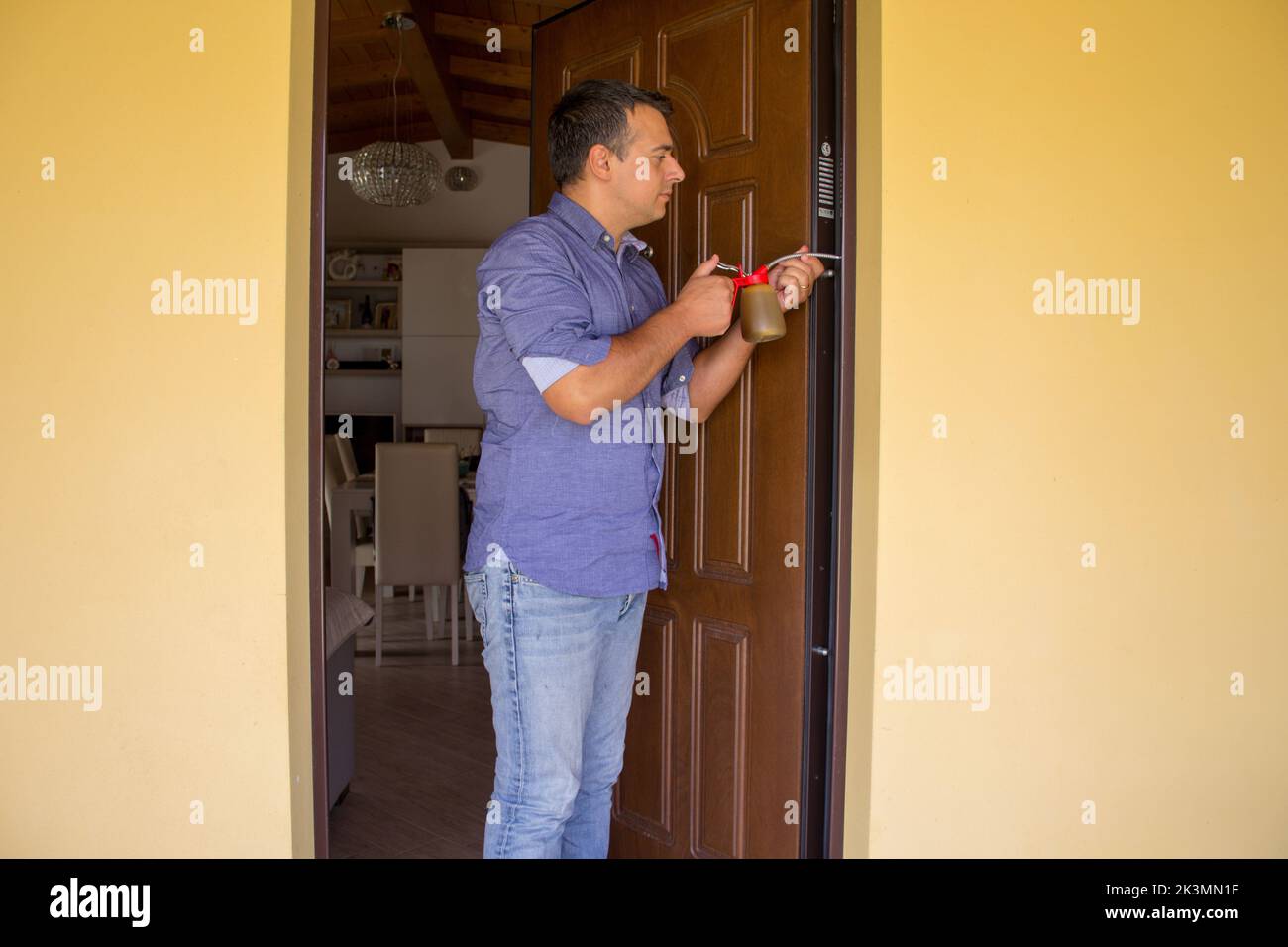 Bild eines Handwerkers, der mit einem Öler die Scharniere einer knarrenden Tür schmiert. Hausarbeit und Do-it-yourself Stockfoto