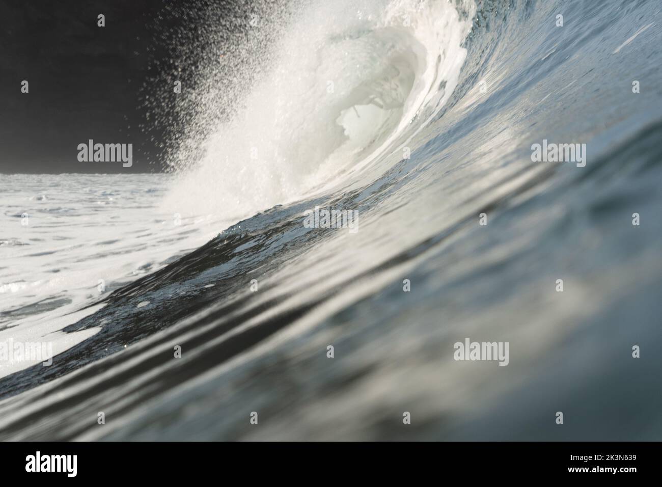 Eine große Welle bricht am Piha Beach, Auckland, Neuseeland. Felsige Landschaft im Hintergrund. Stockfoto