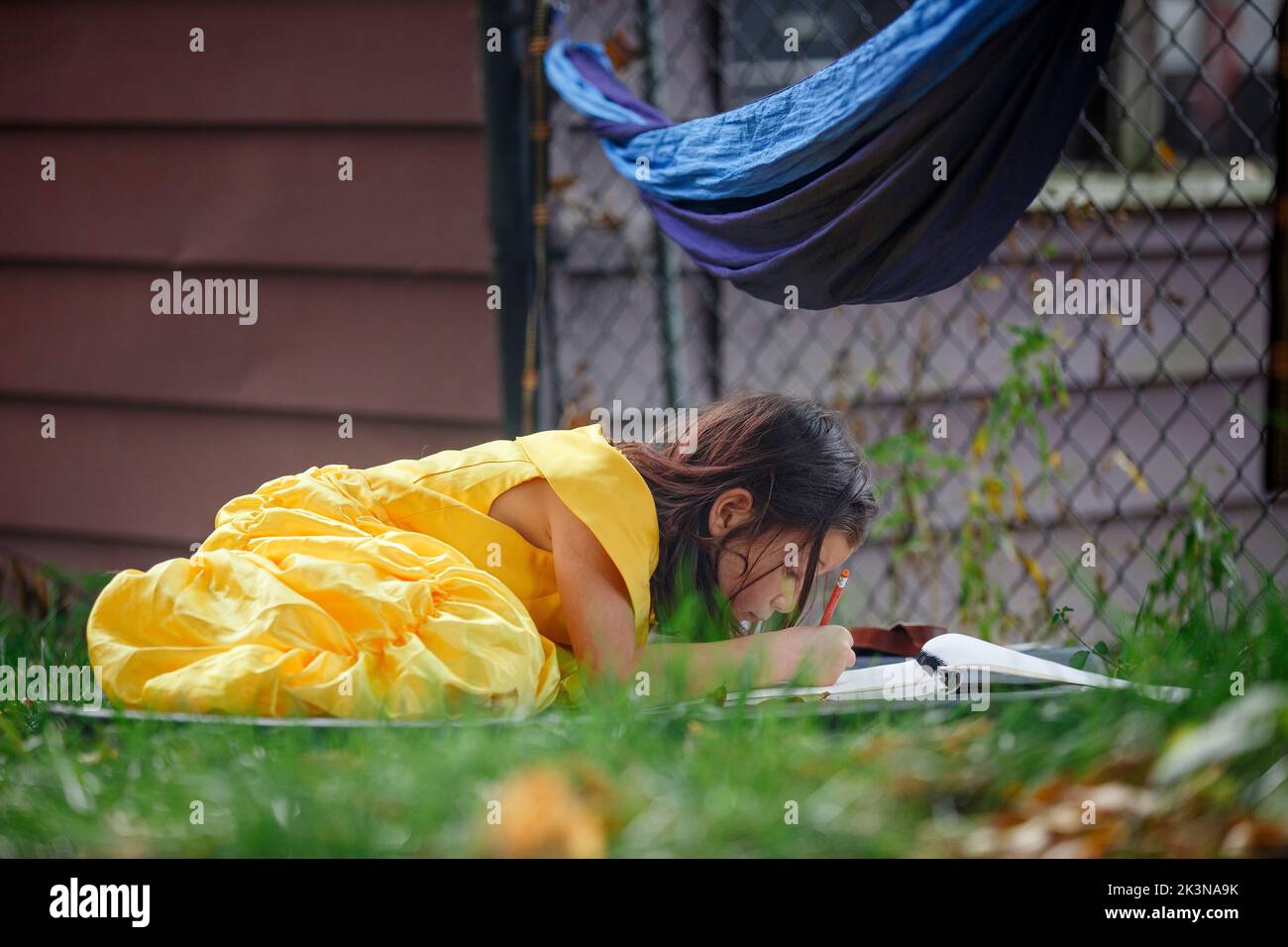 Ein kleines Mädchen in einem leuchtend gelben Kleid liegt in Graszeichnung Stockfoto