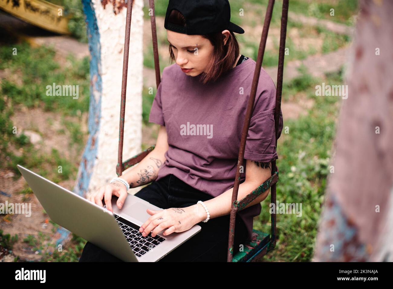 Junge Studentin mit Laptop auf einer Schaukel sitzend Stockfoto