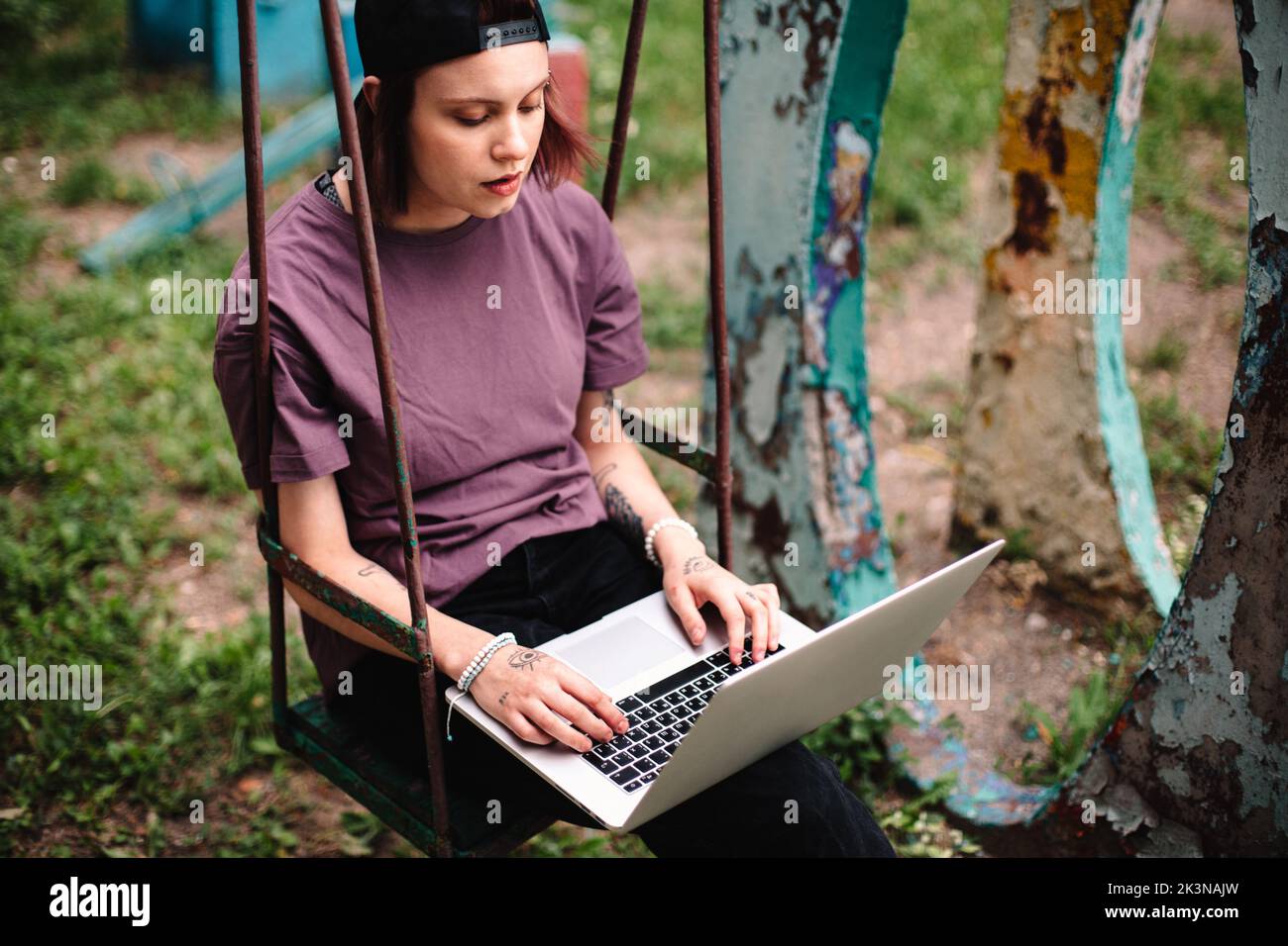 Junge Studentin mit Laptop sitzt im Sommer auf einer Schaukel Stockfoto