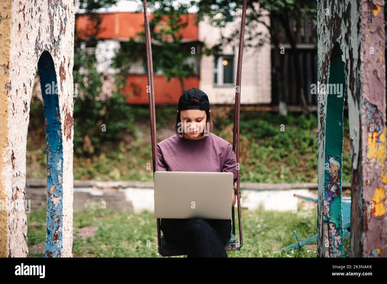 Ernsthafte junge Studentin mit Laptop, die im Sommer auf einer Schaukel sitzt Stockfoto