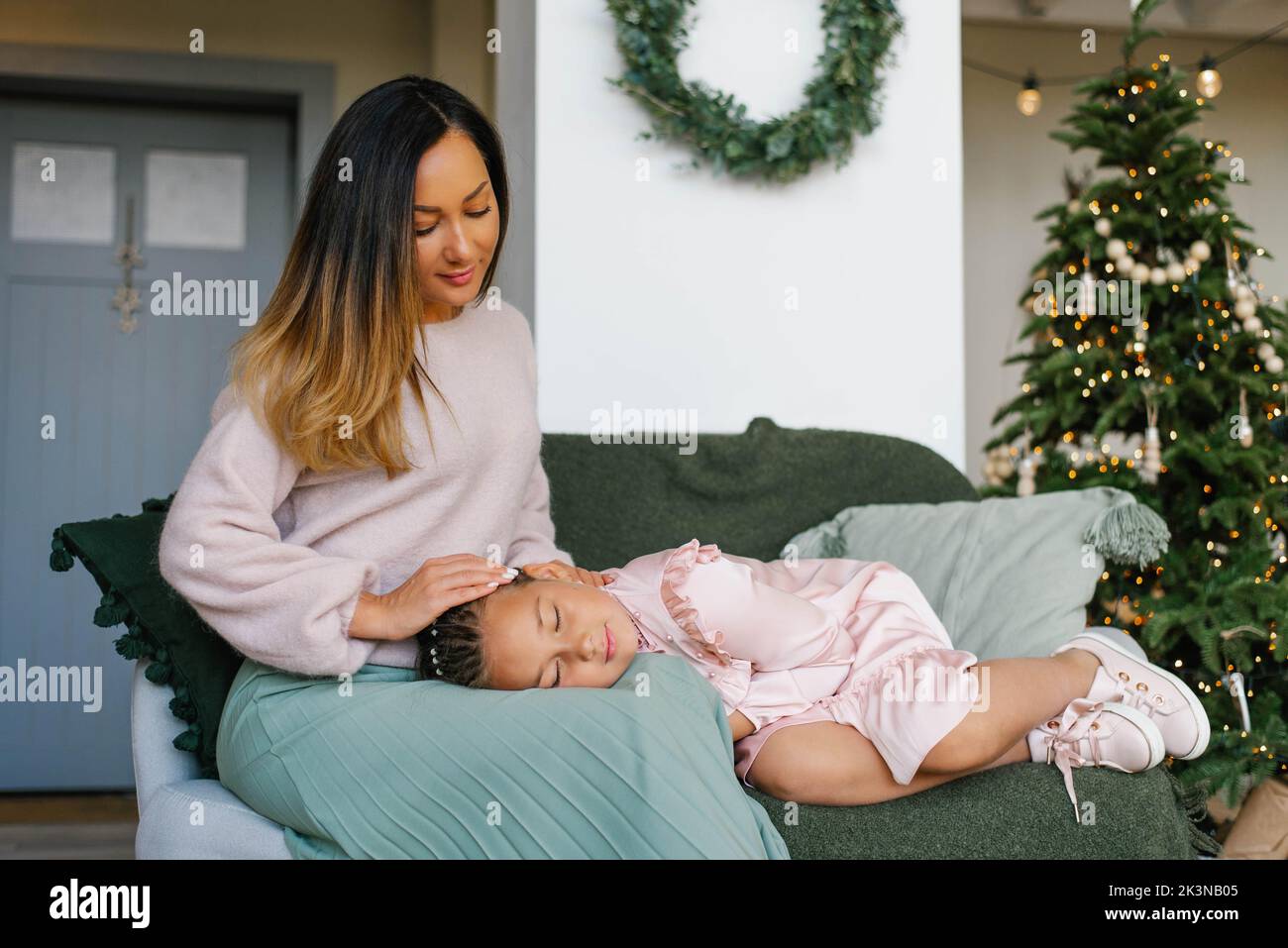 Die Tochter schlief auf dem Schoß ihrer Mutter am Weihnachtsbaum ein Stockfoto