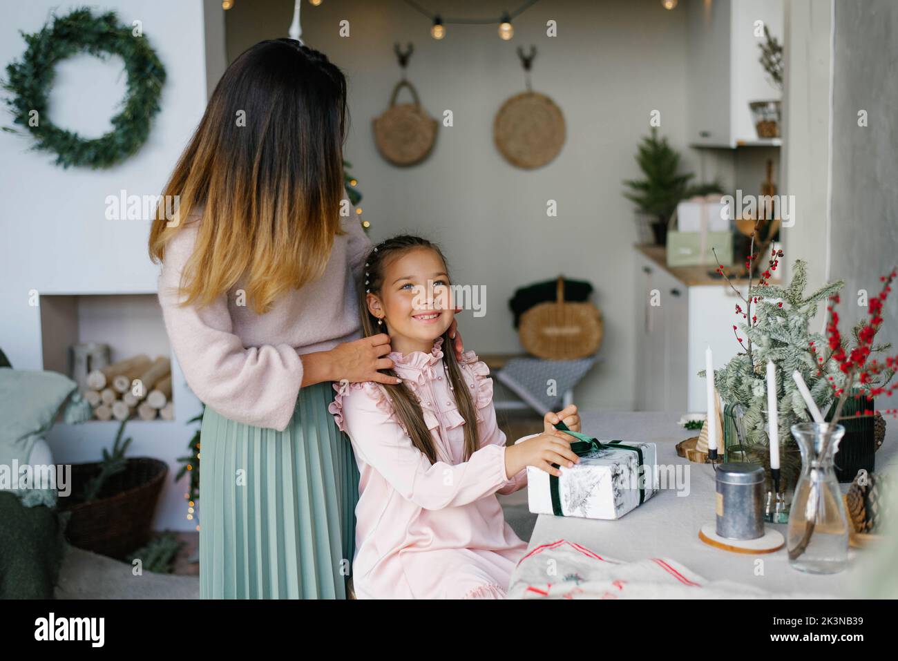 Glückliche und fröhliche Tochter öffnet ein Weihnachtsgeschenk und Mutter umarmt sie Stockfoto