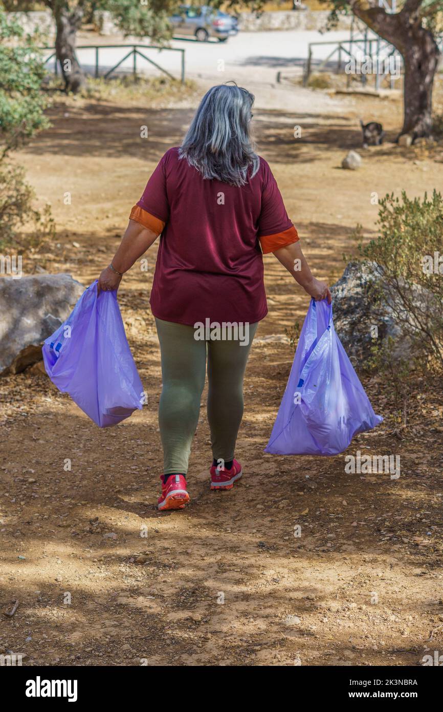 Frau von hinten gesehen, die Müllsäcke trägt, die auf dem Feld gesammelt wurden Stockfoto