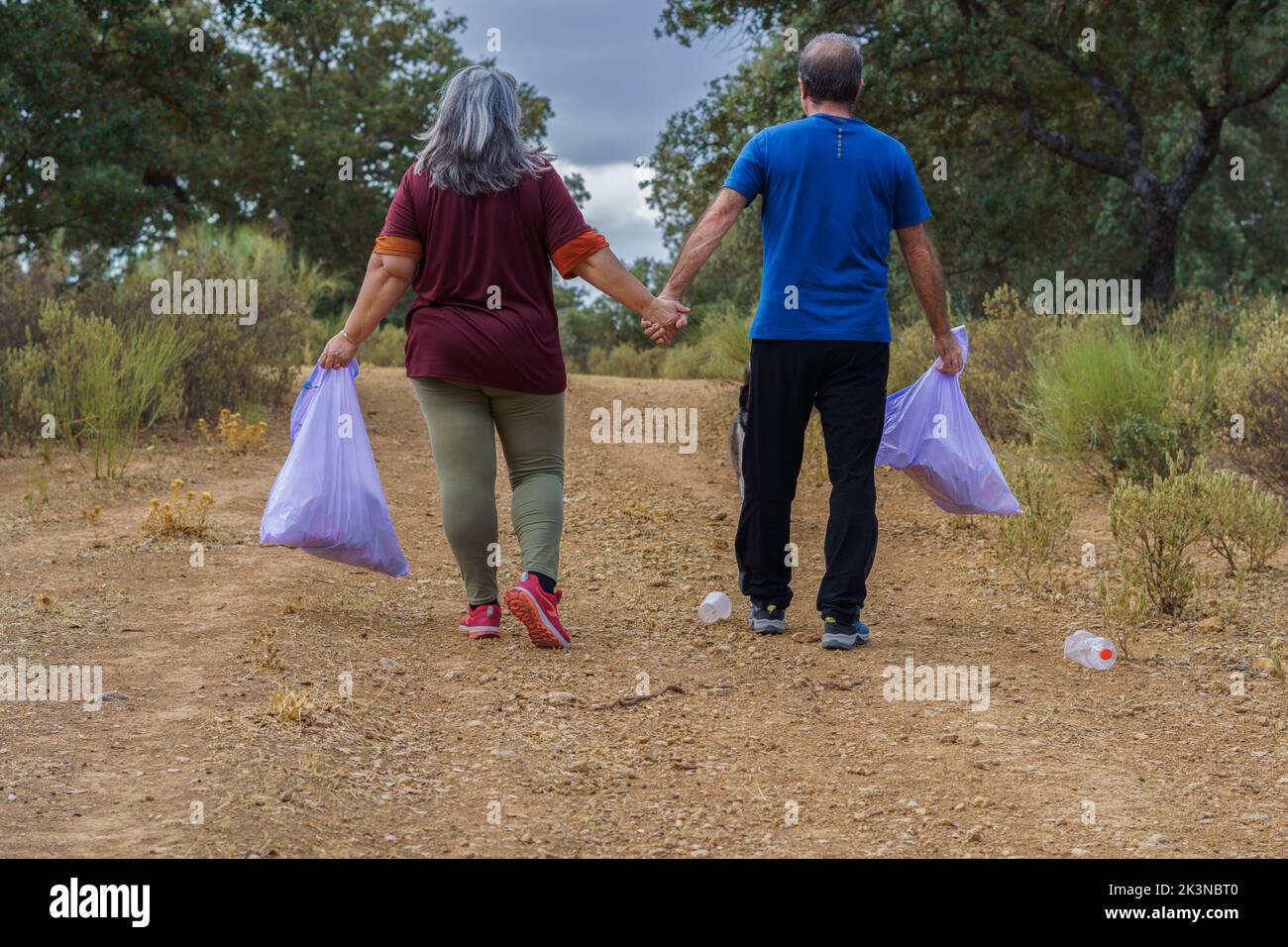 Ein paar Umweltschützer mit Mülltüten, die Hand in Hand gehen Stockfoto