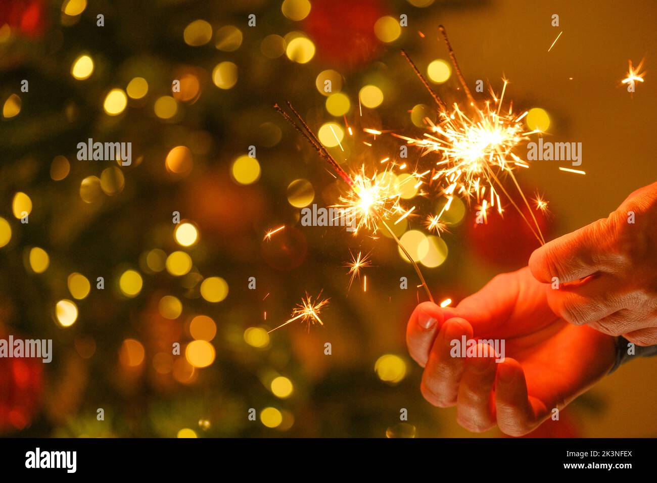 Weihnachtsbeleuchtung.Weihnachts- und Neujahrsparty. Funkelndes bengalisches Feuer in den Händen.Bengalisches Licht auf Girlanden auf einem festlichen Christbaumhintergrund Stockfoto