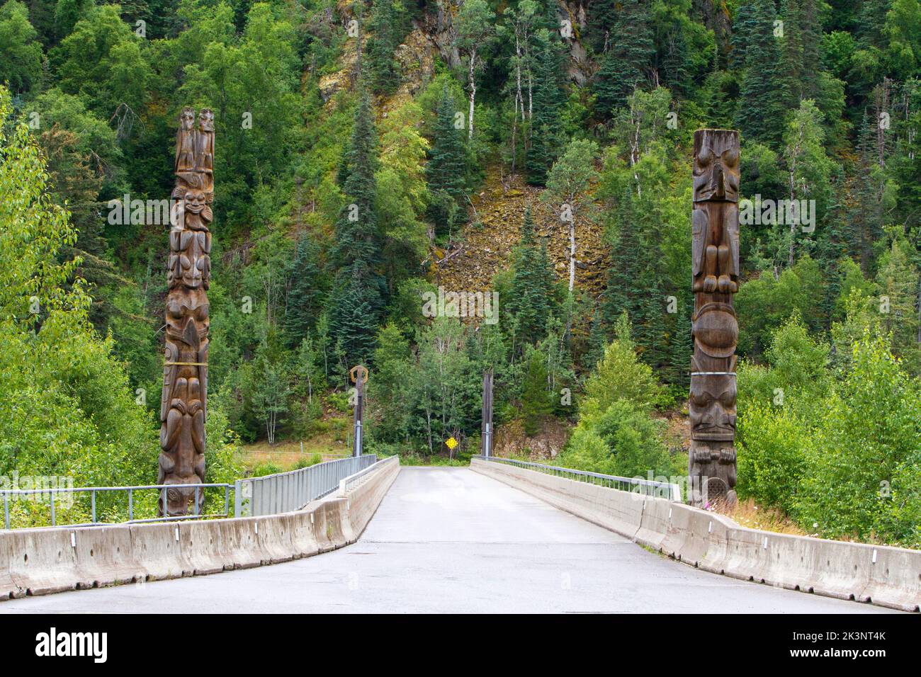 Eine Brücke über den Nass River am Rande des Dorfes Nisga'a in Gitwinksihlkw, British Columbia, Kanada, mit Totempolen auf beiden Seiten. Stockfoto
