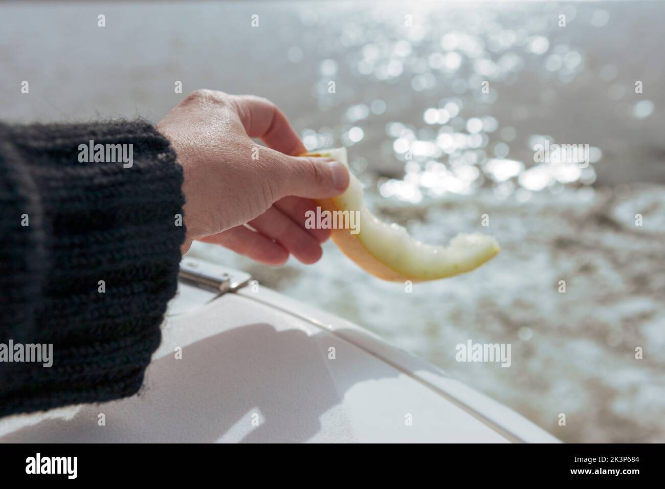 Eine Hand, die eine Melonenhaut in eine sonnige Tagesaufnahme wirft Stockfoto
