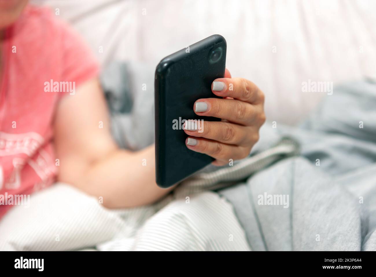 Frau mit gepflegten Nägeln hält ihr Smartphone, während sie auf einem Sofa sitzt Stockfoto