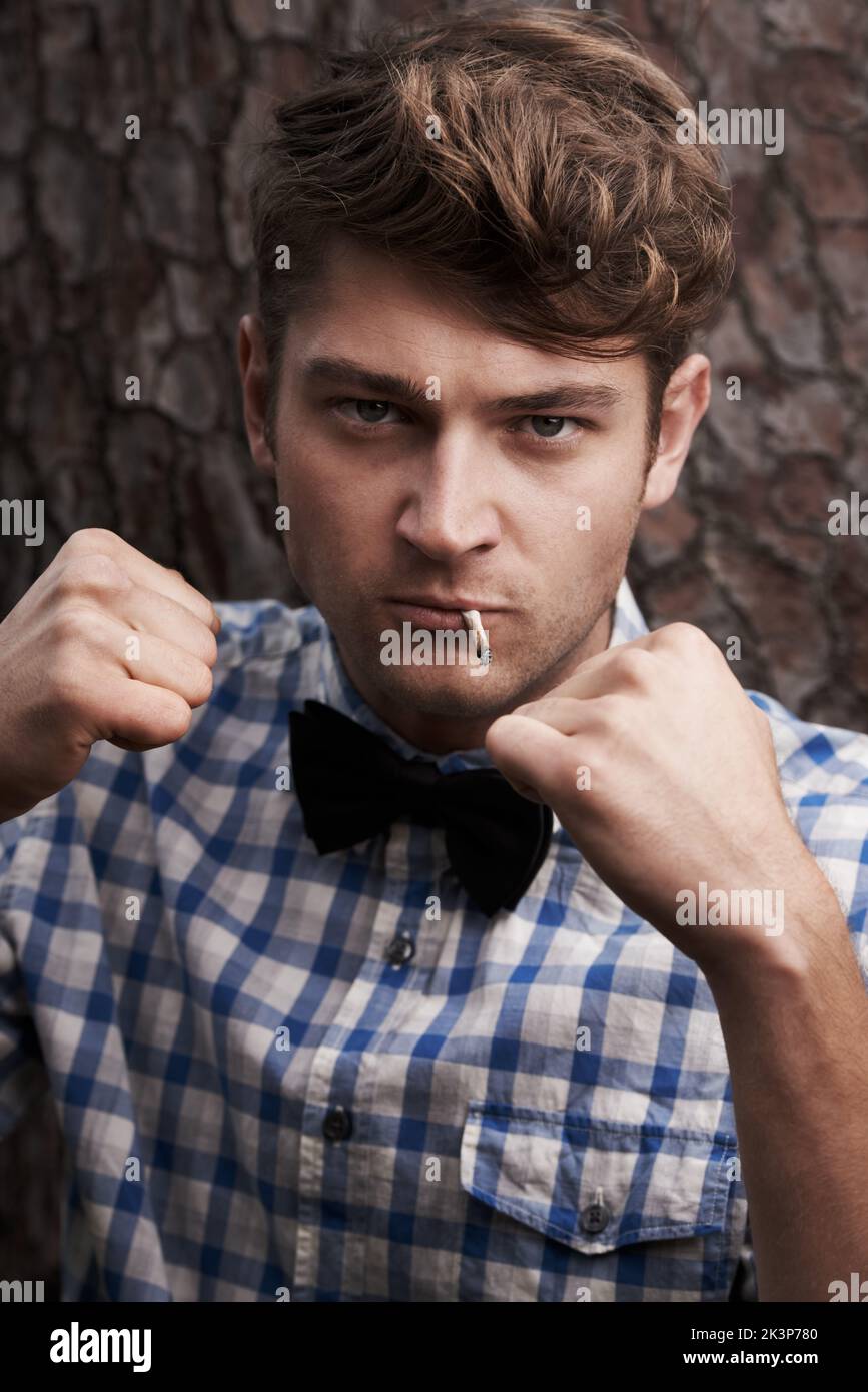 Style mit einer rauen Kante. Porträt eines schlauen jungen Mannes mit erhobenen Armen in einer kämpfenden Pose, der vor einem Baum steht. Stockfoto