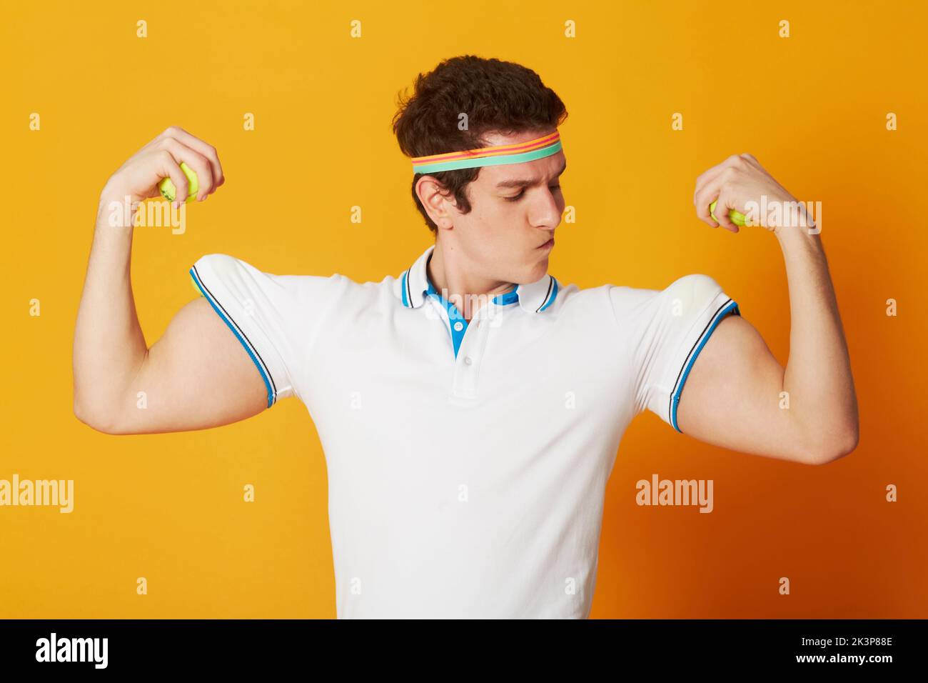 Meine Muskeln sind real, schwöre ich. Ein kaukasischer Mann, der Tennisbälle als Muskel für seine Arme verwendet, während er eine alberne Pose in Tenniskleidung zieht. Stockfoto Meine Muskeln sind real, schwöre ich. Ein kaukasischer Mann, der Tennisbälle als Muskel für seine Arme verwendet, während er eine alberne Pose in Tenniskleidung zieht. Stockfoto
