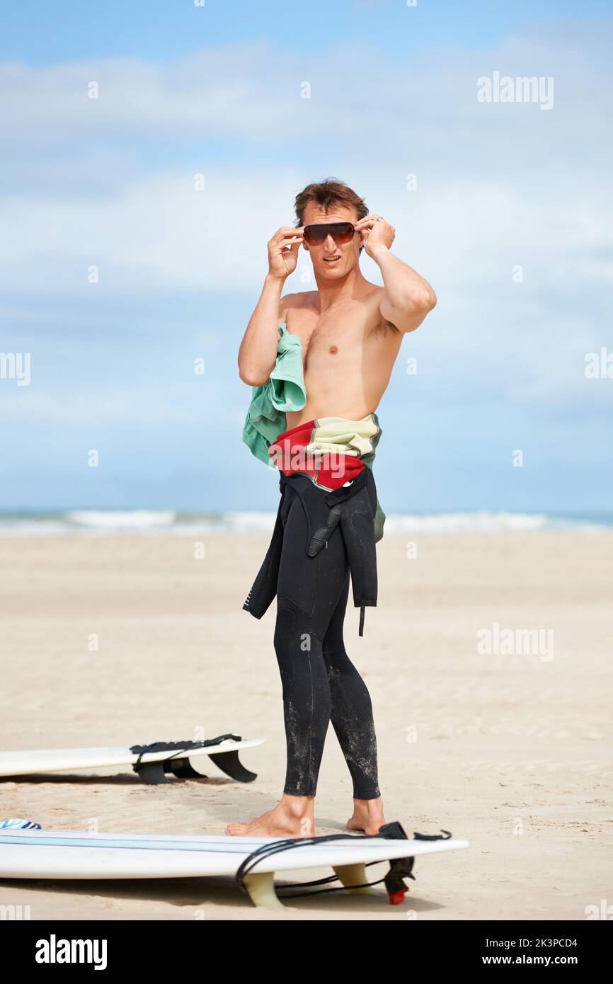 Surfer-Typ. Die ganze Länge eines jungen Surfers, der am Strand steht und seine Schattierungen aufsetzt. Stockfoto