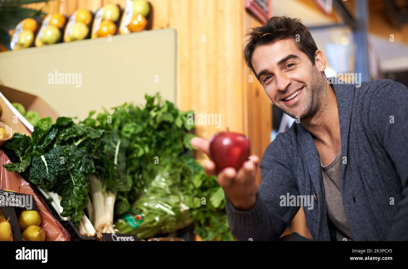 Wie wäre es mit diesem einen. Ein hübscher junger Mann, der auf einem Markt einkauft und einen Apfel an die Kamera hält. Stockfoto