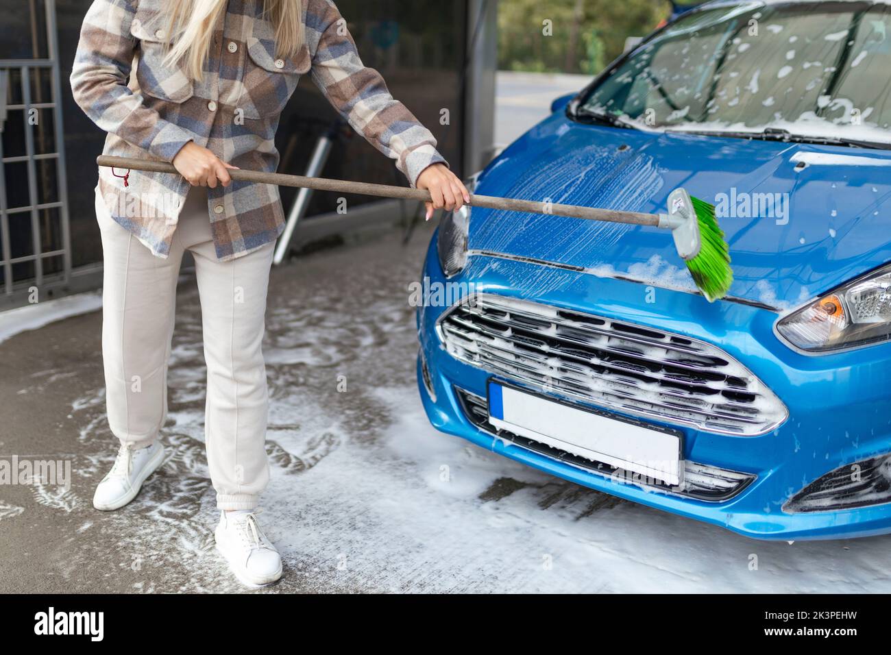 Die Frauen selbst bei der Waschanlage wäscht das Auto mit einer Bürste Stockfoto