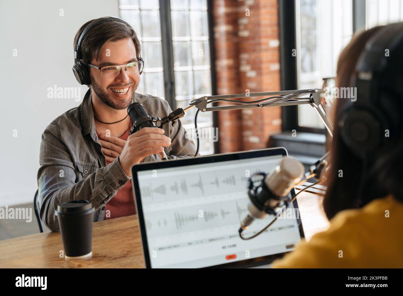 Podcast-Inhalte. Aufgeregter, gutaussehender männlicher Gast, der eine Gastgeberin anschaut, während sie im Studio einen Audio-Podcast macht. Zwei Podcasts in Kopfhörern lachen, reden, nehmen Live-Podcasts auf Stockfoto