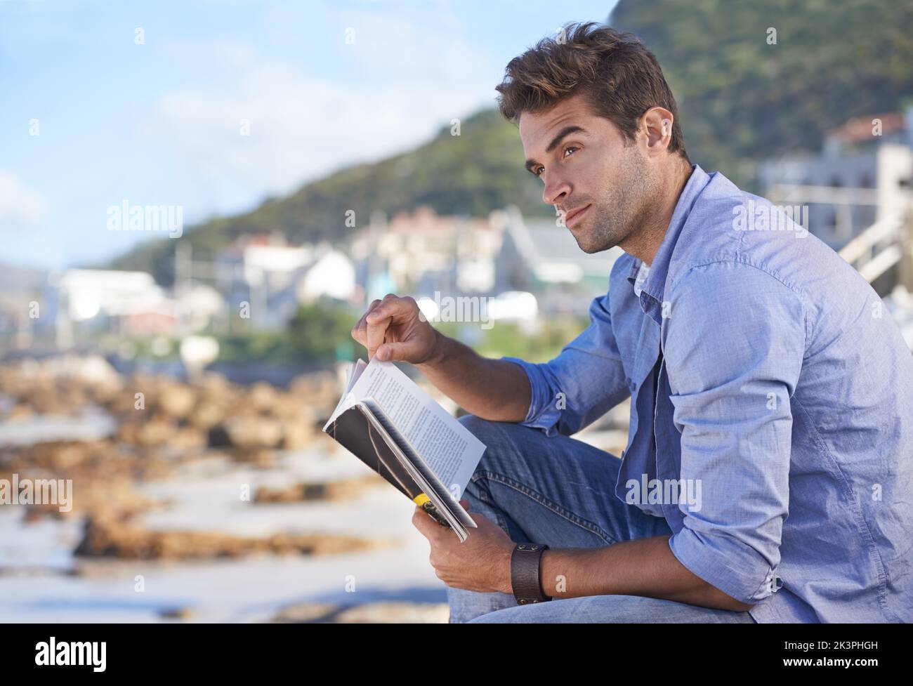 Romane sind eine großartige Möglichkeit, sich zu entspannen. Ein junger Mann, der im Freien ein Buch liest. Stockfoto