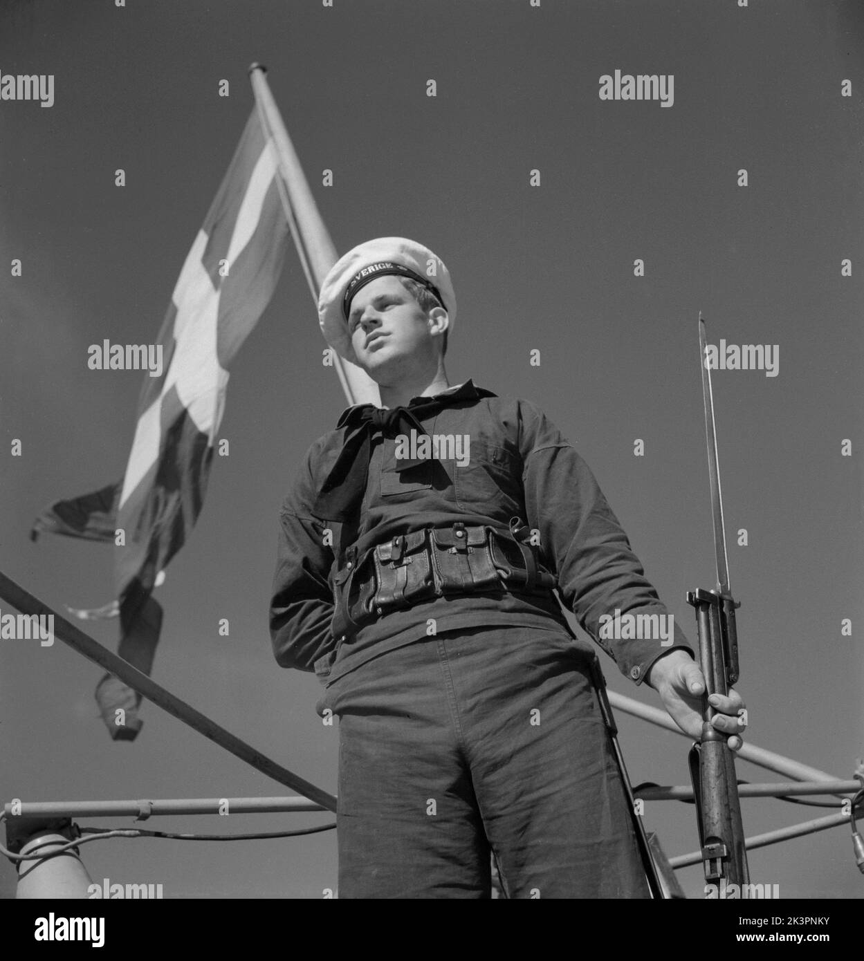 Während des Zweiten Weltkriegs Das Kriegsschiff Sverige während der Marineübungen auf See. Detail eines Matrosen, der auf dem Schiff mit einem Gewehr in der Hand steht. Die schwedische Marineflagge ist im Hintergrund zu sehen. Schweden juni 1940. Kristoffersson Ref. 141 Stockfoto