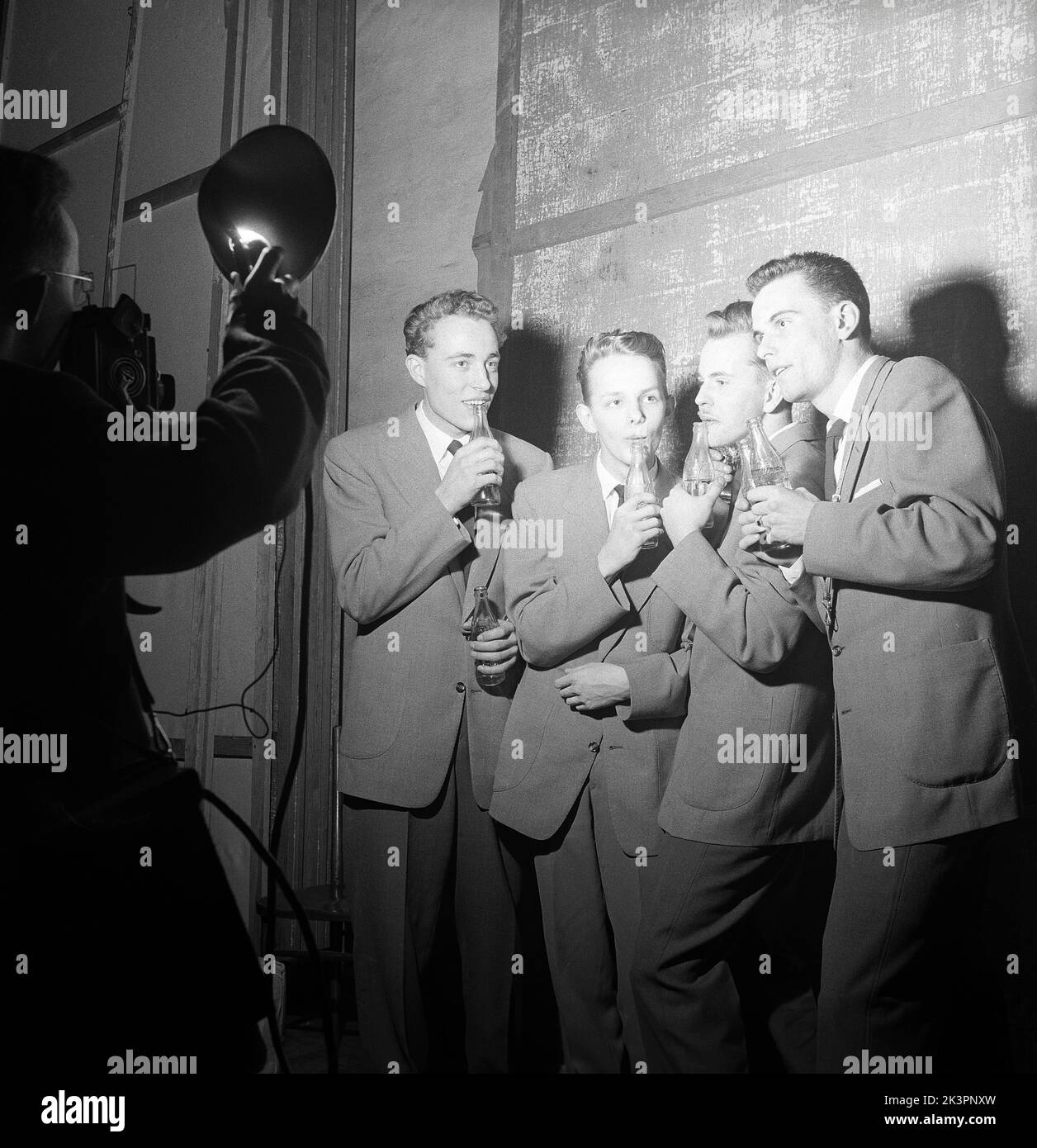 1950s Talente. Eine Gruppe von vier jungen Männern tritt in eine Talentshow ein und spielt Musik, die in Coca-Cola-Flaschen weht. Da die Flaschen mit unterschiedlichen Wasserständen gefüllt sind, machen sie beim Aufblasen unterschiedliche Geräusche, genug scheint es, ein Musikstück lang genug zu machen, um damit aufzutreten. Beachten Sie den Trick des Fotografen, andere Fotografen Lichter zu verwenden. Schweden 1954 Kristoffersson Ref. BX36-4 Stockfoto