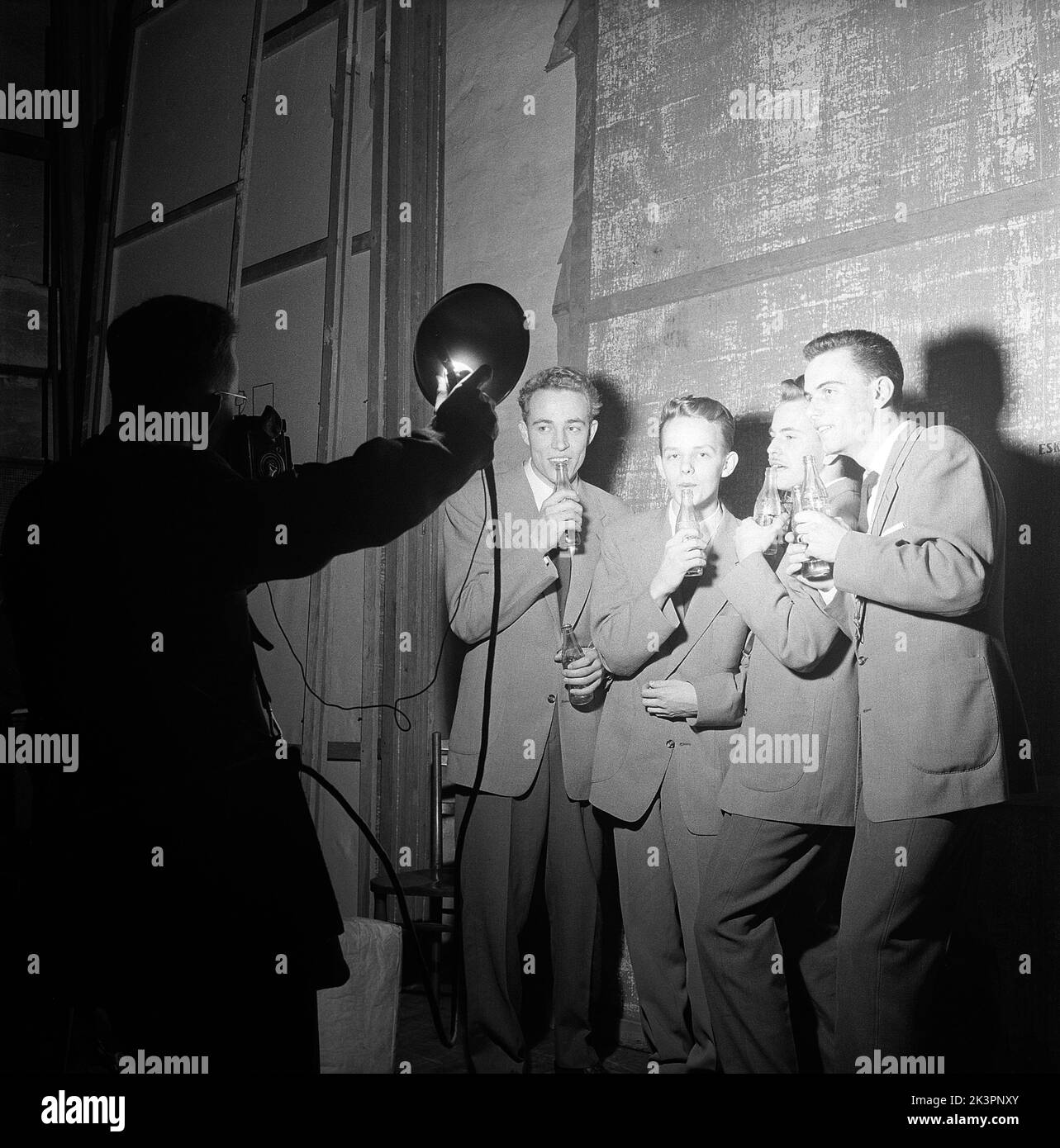 1950s Talente. Eine Gruppe von vier jungen Männern tritt in eine Talentshow ein und spielt Musik, die in Coca-Cola-Flaschen weht. Da die Flaschen mit unterschiedlichen Wasserständen gefüllt sind, machen sie beim Aufblasen unterschiedliche Geräusche, genug scheint es, ein Musikstück lang genug zu machen, um damit aufzutreten. Beachten Sie den Trick des Fotografen, andere Fotografen Lichter zu verwenden. Schweden 1954 Kristoffersson Ref. BX37-12 Stockfoto