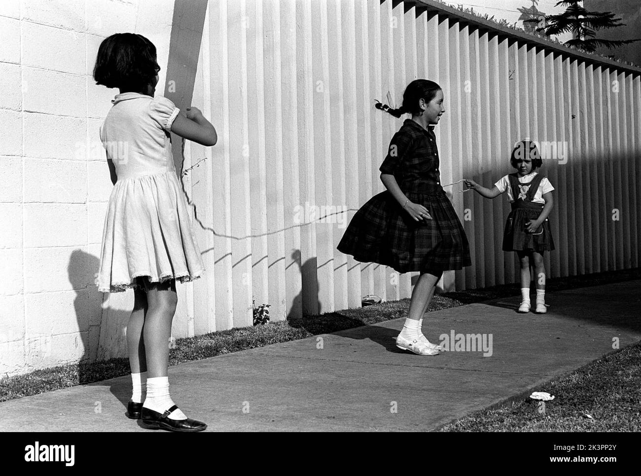 Mexiko im Jahr 1960s. Drei Mädchen spielen auf der Straße, mit einem Springseil - einem Springseil. Ein Mädchen an jedem Ende des Seils schwingt es und ein Mädchen in der Mitte springt darüber. Mexiko 1964. Roland Palm Ref.-Ordner 2 Stockfoto