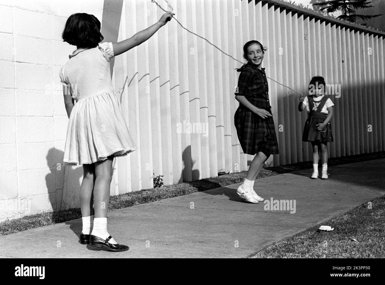 Mexiko im Jahr 1960s. Drei Mädchen spielen auf der Straße, mit einem Springseil - einem Springseil. Ein Mädchen an jedem Ende des Seils schwingt es und ein Mädchen in der Mitte springt darüber. Mexiko 1964. Roland Palm Ref.-Ordner 2 Stockfoto