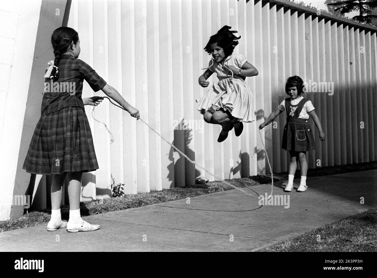 Mexiko im Jahr 1960s. Drei Mädchen spielen auf der Straße, mit einem Springseil - einem Springseil. Ein Mädchen an jedem Ende des Seils schwingt es und ein Mädchen in der Mitte springt darüber. Mexiko 1964. Roland Palm Ref.-Ordner 2. Stockfoto