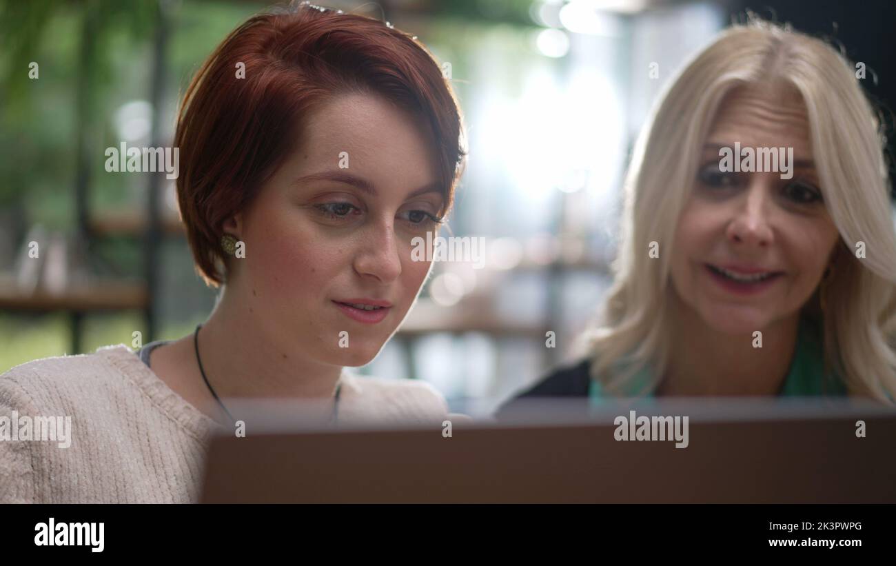 Zwei Menschen in verschiedenen Altersgruppen betrachten Computerbildschirm. Glückliche Arbeiterinnen, die zusammen einen Laptop benutzen, Portraitgesichter aus der Nähe Stockfoto