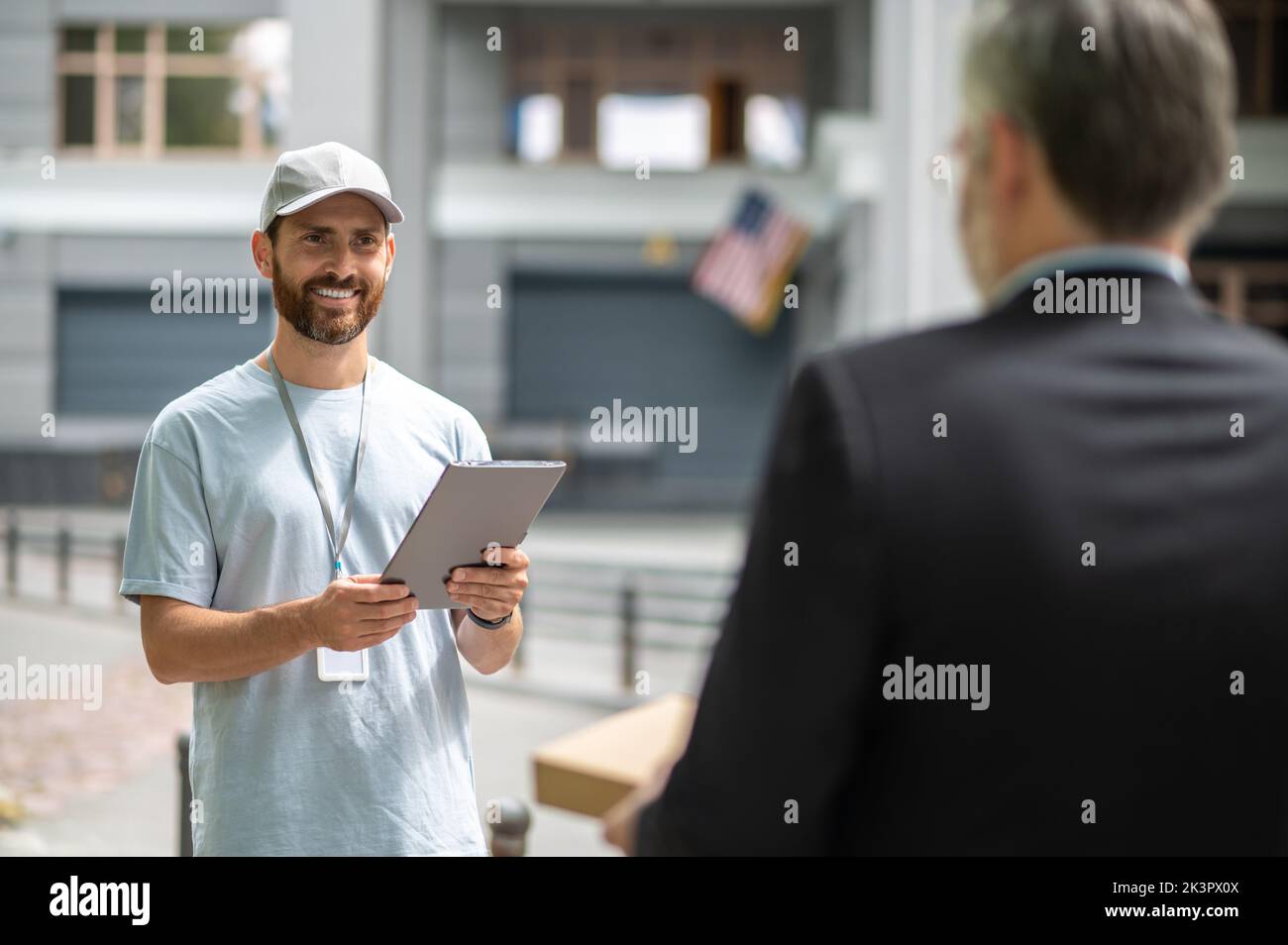 Ein Courrier in einer Mütze, der dem Mann in einem Suuit eine Schachtel gibt Stockfoto