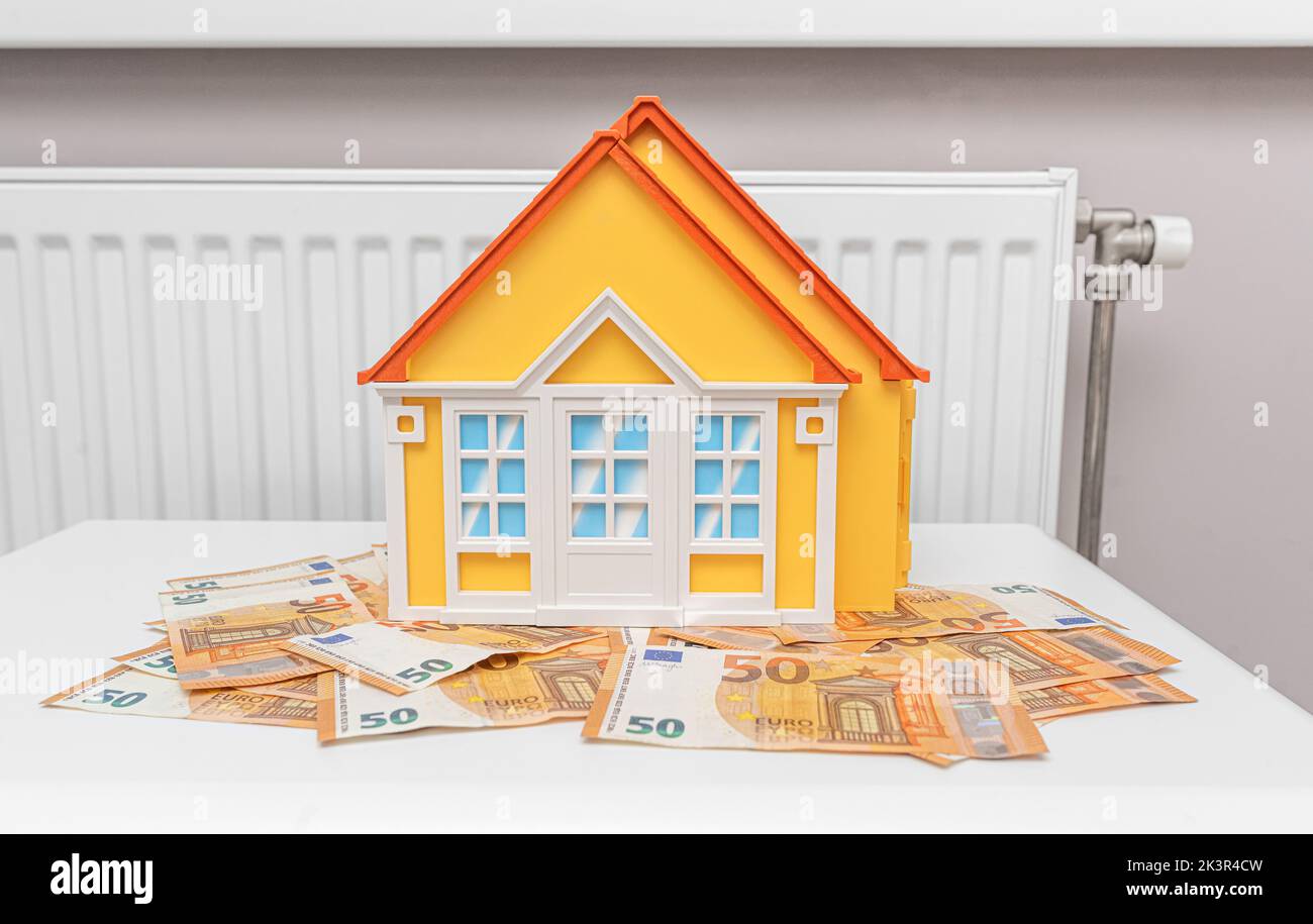 Das Modell des Hauses steht auf Banknoten vor dem Hintergrund eines Heizkörpers. Stockfoto