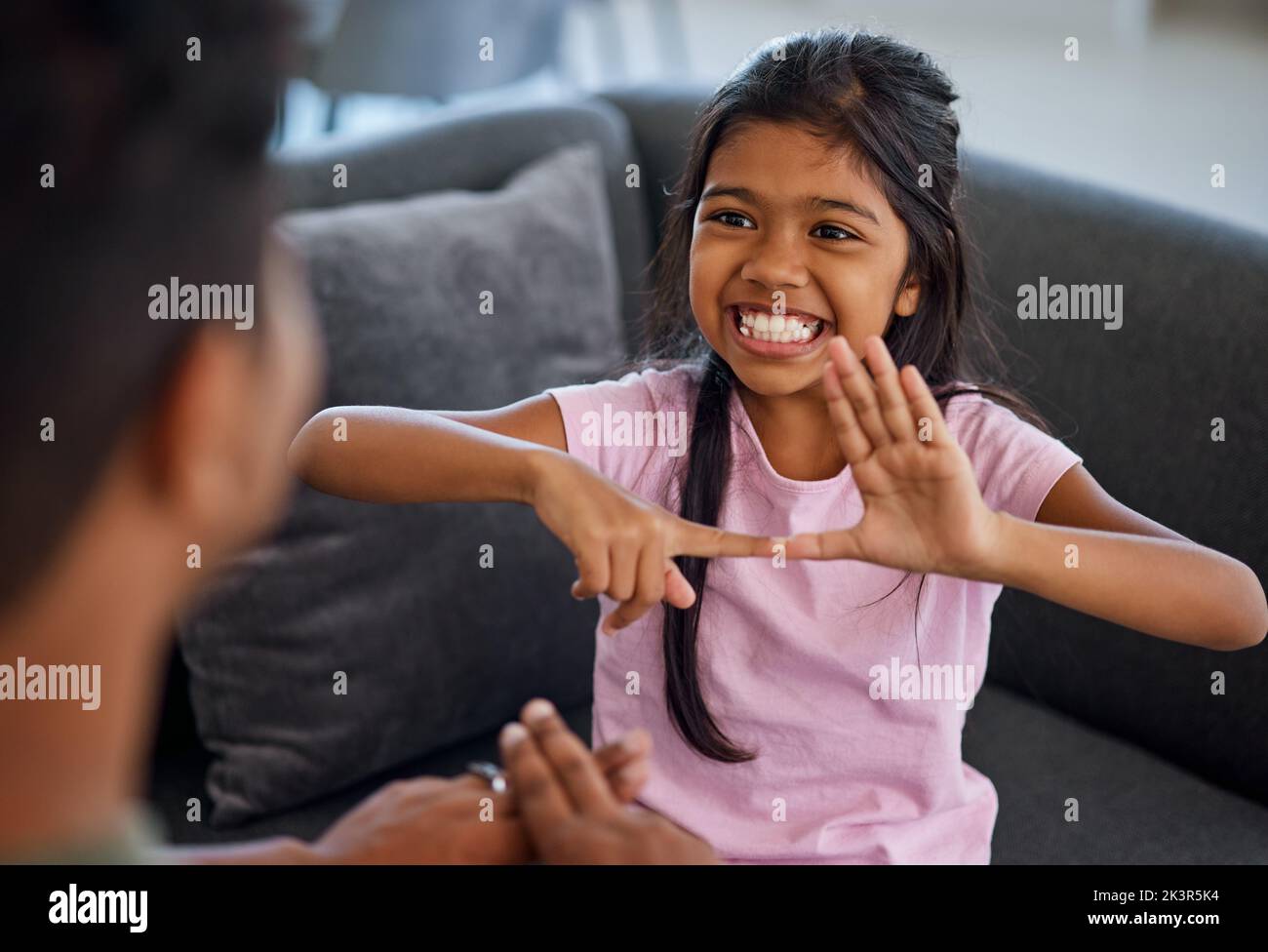 Kind, Gebärdensprache und lernen, mit gehörlosen Mädchen oder Eltern zu kommunizieren, während man Finger macht und visuelle Symbole zu Hause zeigt. Glückliches Kind mit Stockfoto