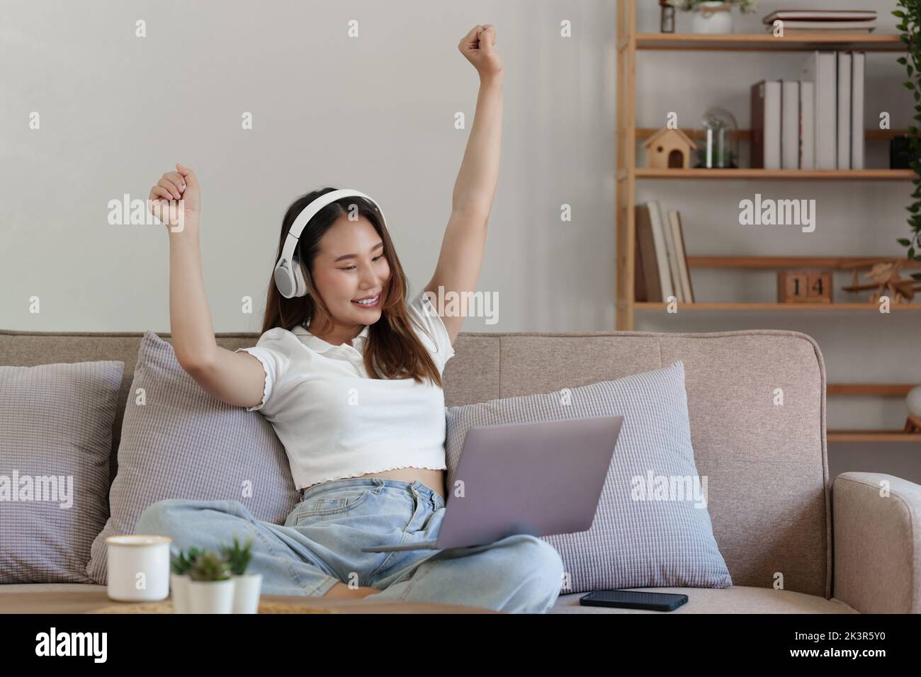 Attraktive lächelnde junge Frau mit Laptop und Musik hören auf dem Sofa zu Hause. Lifestyle-Konzept Stockfoto