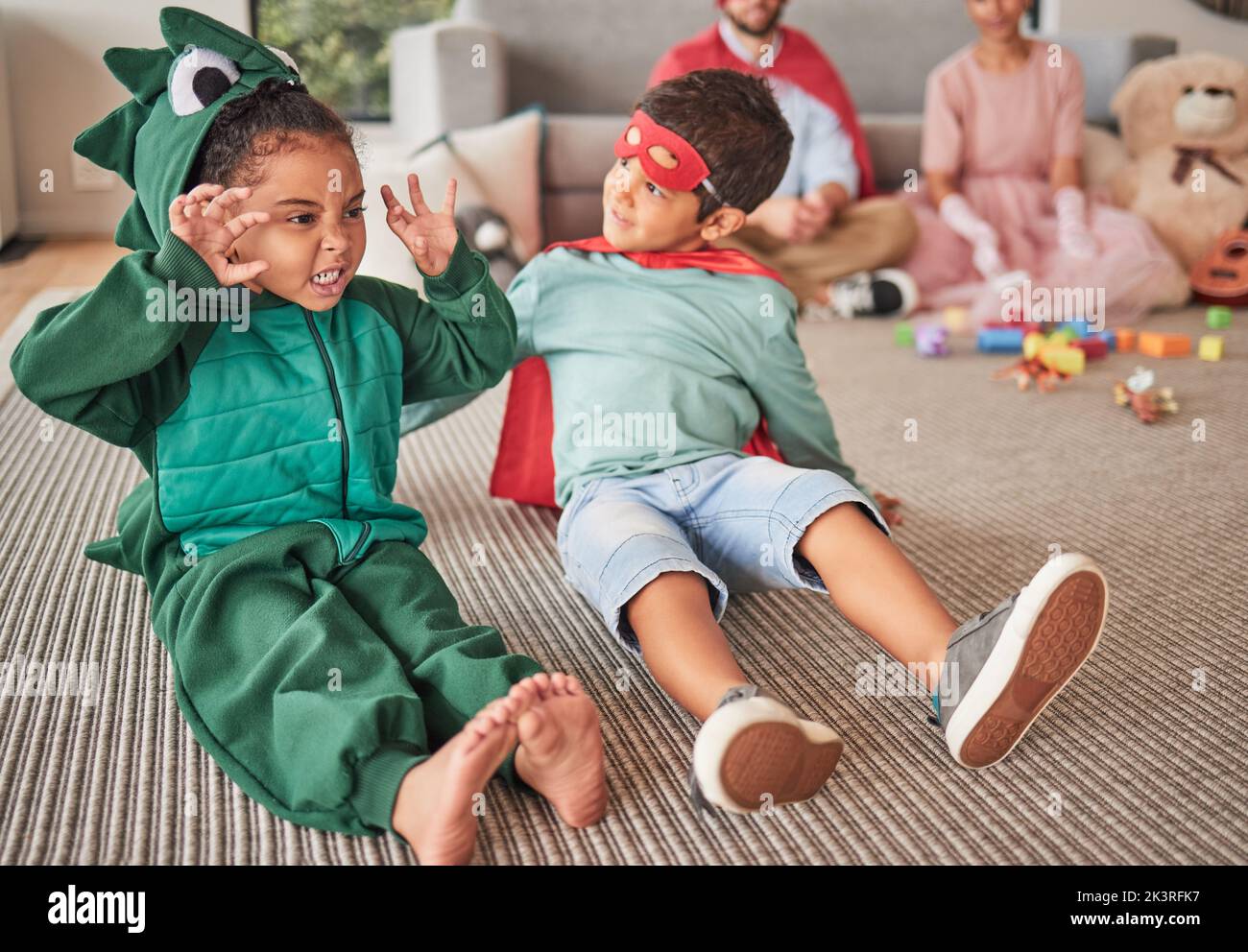 Familie, halloween und Kinder, die in Kostümen auf einem Boden im Wohnzimmer spielen, Spaß haben und kreativ sein. Superhelden, Dinosaurier und kreative Kinder Stockfoto