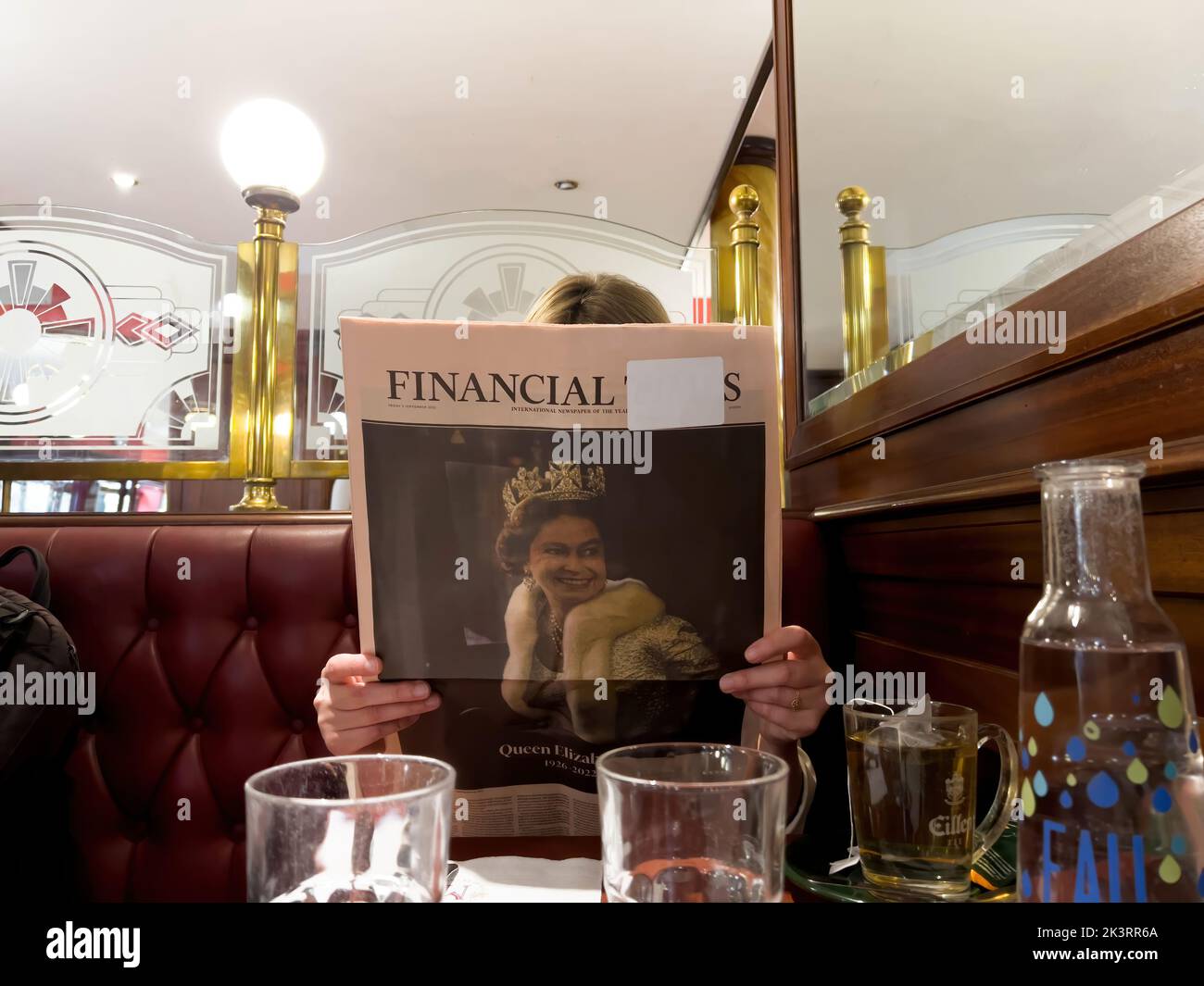 London, Vereinigtes Königreich - 9. Sep 2022: Junge Frau liest im Pub Cafe Englische Zeitung Financial Times zollt der Königin Tribut nach ihrem Tod - Königin Elizabeth II starb im Balmoral Castle in Schottland Stockfoto