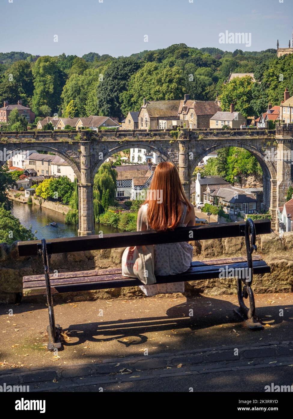Frau, die auf einer Bank sitzt und den Blick auf den Eisenbahnviadukt über den Fluss Nidd in Knaresborough North Yorkshire England genießt Stockfoto