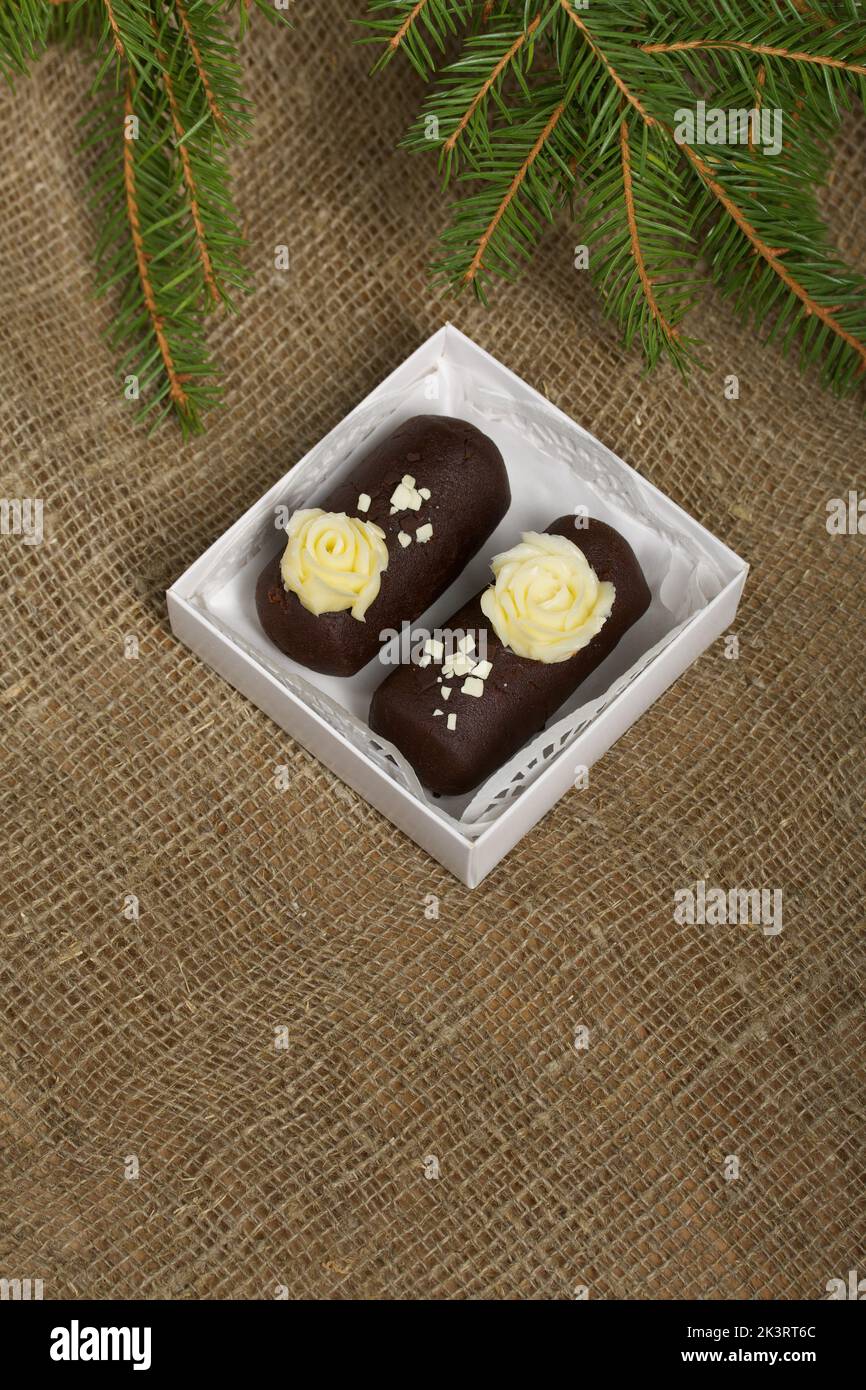 Tortenkartoffel. Dekoriert mit Buttercreme. In einer Geschenkbox. Auf Leinenhintergrund. Neben einem Fichtenzweig. Nahaufnahme. Stockfoto