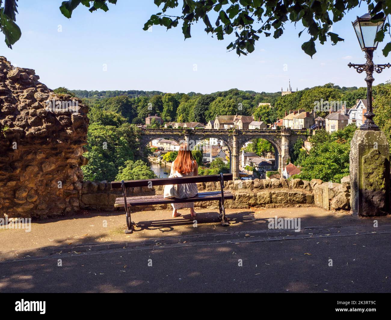 Frau, die auf einer Bank sitzt und den Blick auf den Eisenbahnviadukt über den Fluss Nidd in Knaresborough North Yorkshire England genießt Stockfoto