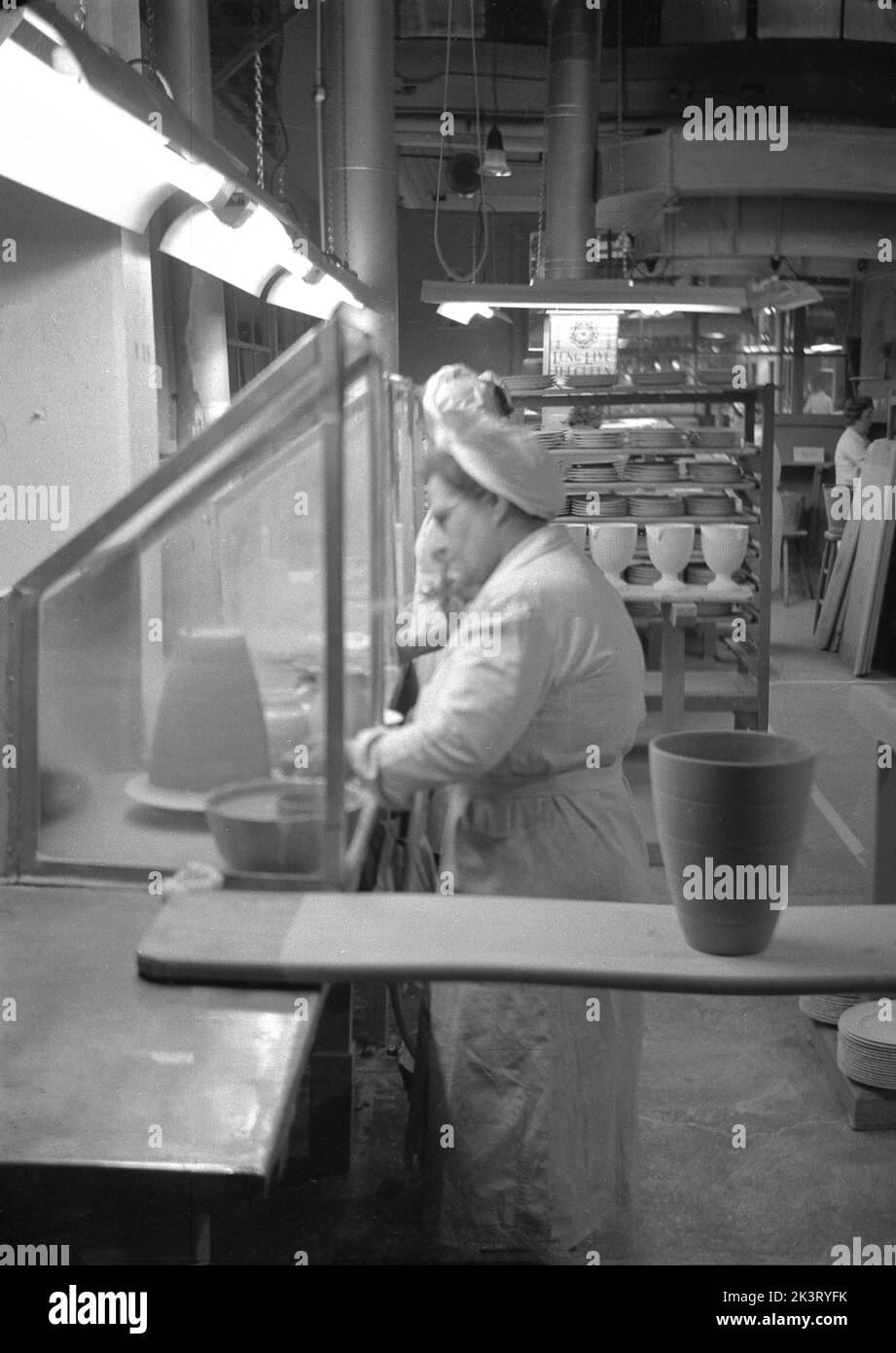 1950er Jahre, historisch, in der Fabrikhalle, eine Arbeiterin in in einem Overall und Haarnetz Herstellung von Töpferwaren bei Josiah Wedgwood & Sons Ltd. In Barlaston, Stoke-on-Trent, England, Großbritannien Stockfoto