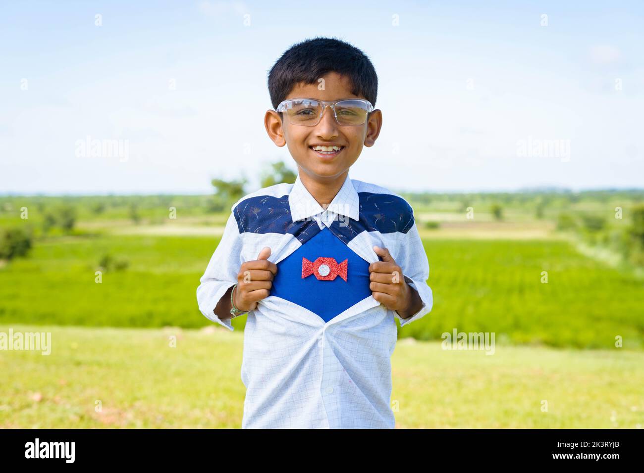 Glücklich lächelndes indisches Teenager-Kind zeigt Supermacht durch Ausziehen des Hemdes durch Blick auf die Kamera - Konzept der Inspiration, Stärke und Glück. Stockfoto