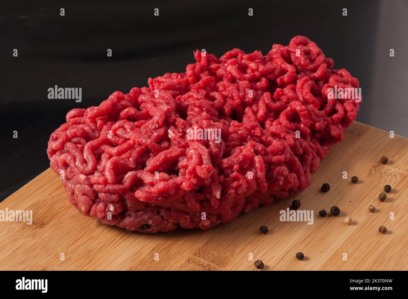 Frisches rohes Hackfleisch auf einem Holzbrett mit schwarzem Pfeffer Stockfoto