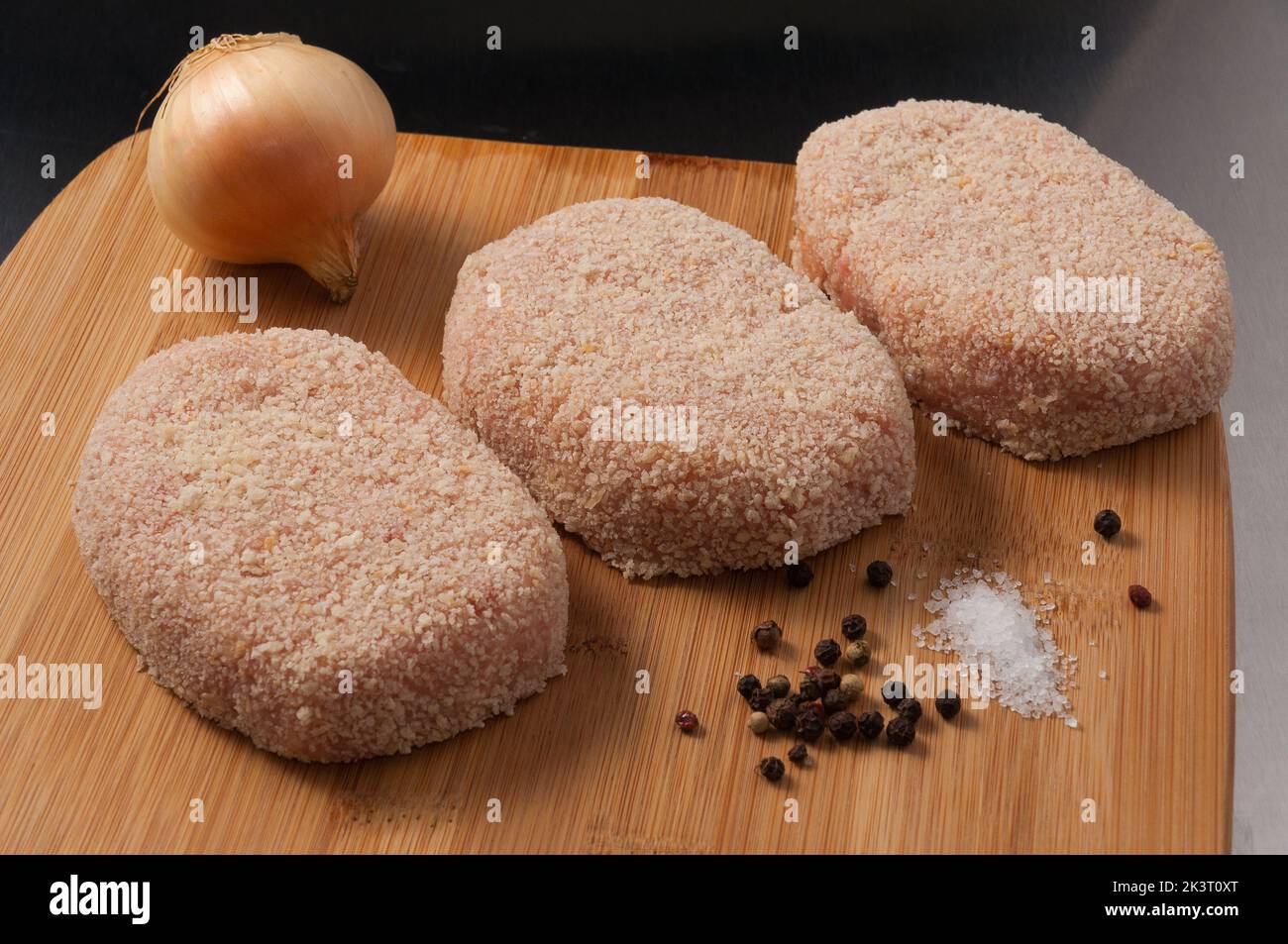 Leckere rohe Hähnchenschnitzel in Semmelbröseln auf einem Holzbrett Stockfoto