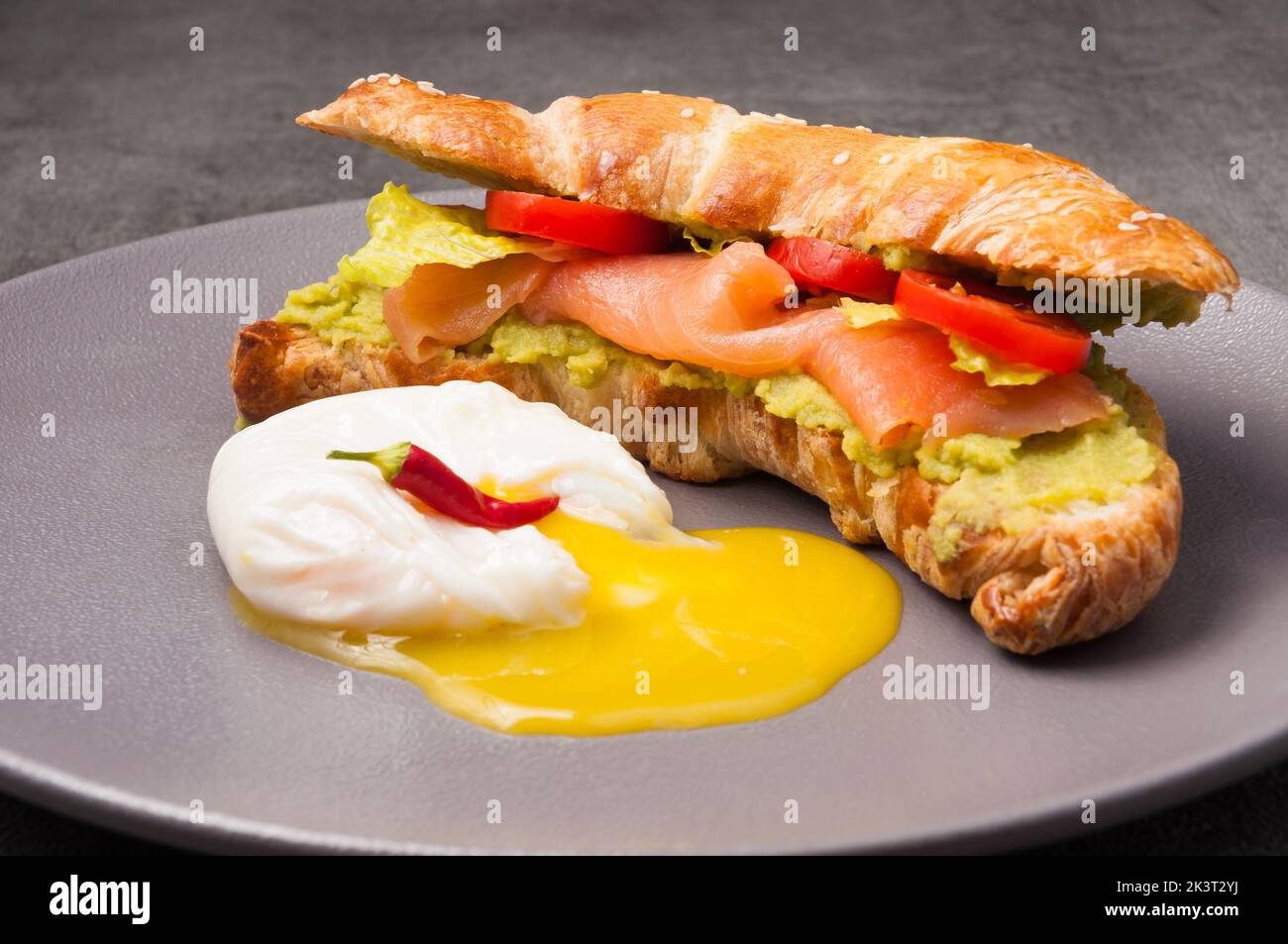 Leckeres Croissant mit Lachs, Avocado-Paste und pochiertem Ei Stockfoto