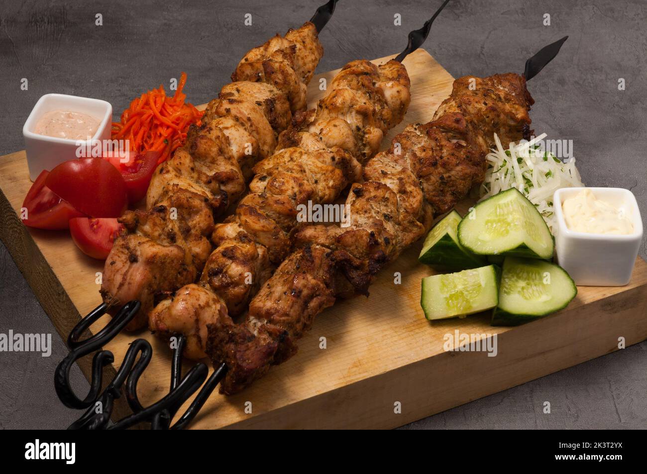 Leckere, sortierte Kebabs auf Metallspiessen mit Gemüse und Saucen Stockfoto